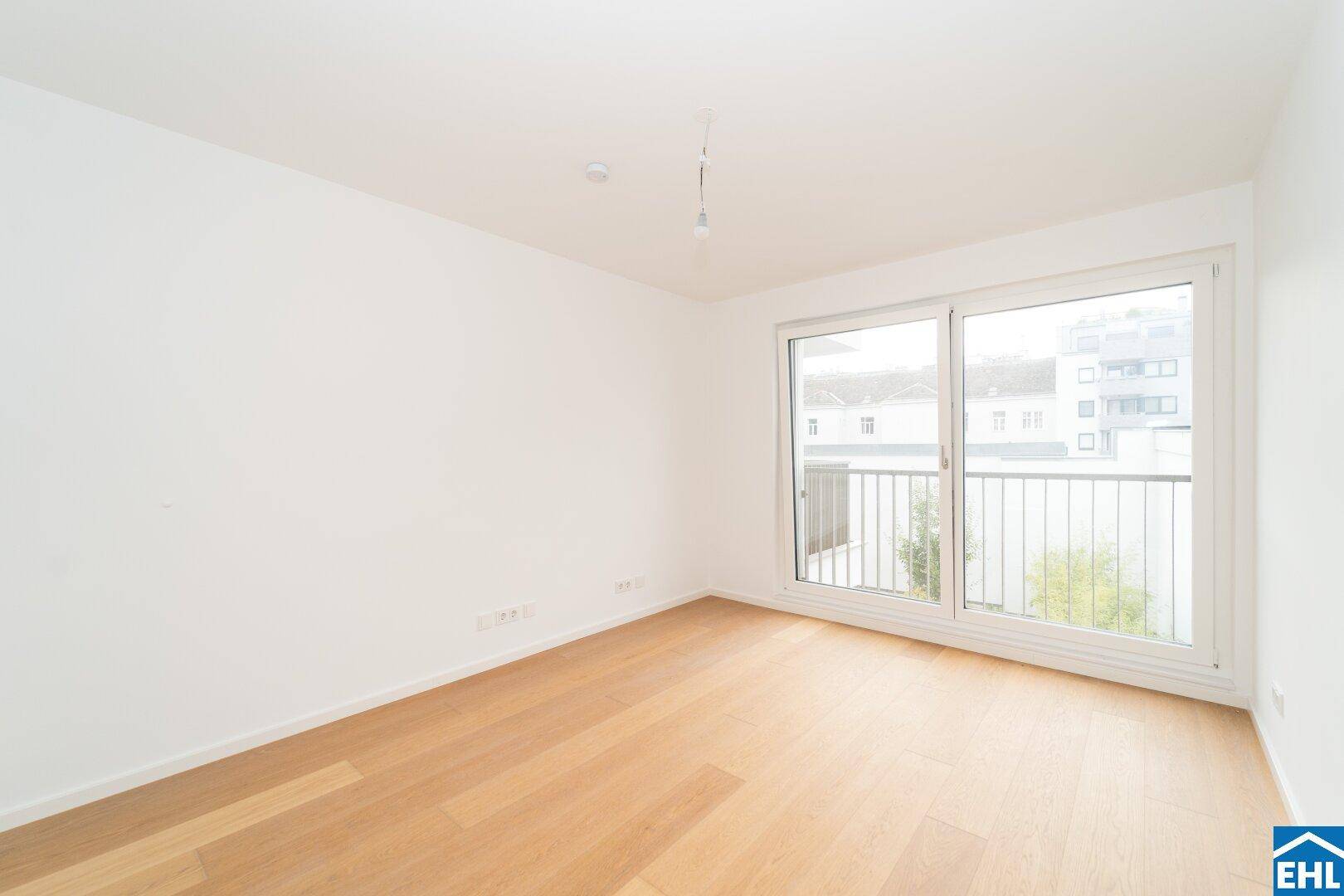 Leeres Schlafzimmer mit Holzboden und großen Fenstern, die viel Tageslicht hereinlassen.