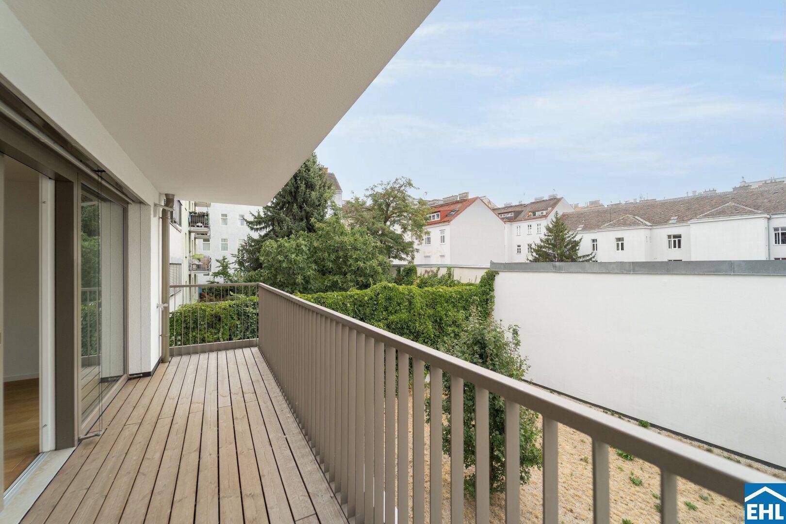 Geräumiger Balkon mit Holzbelag und Blick auf grüne Bäume und umliegende Gebäude.