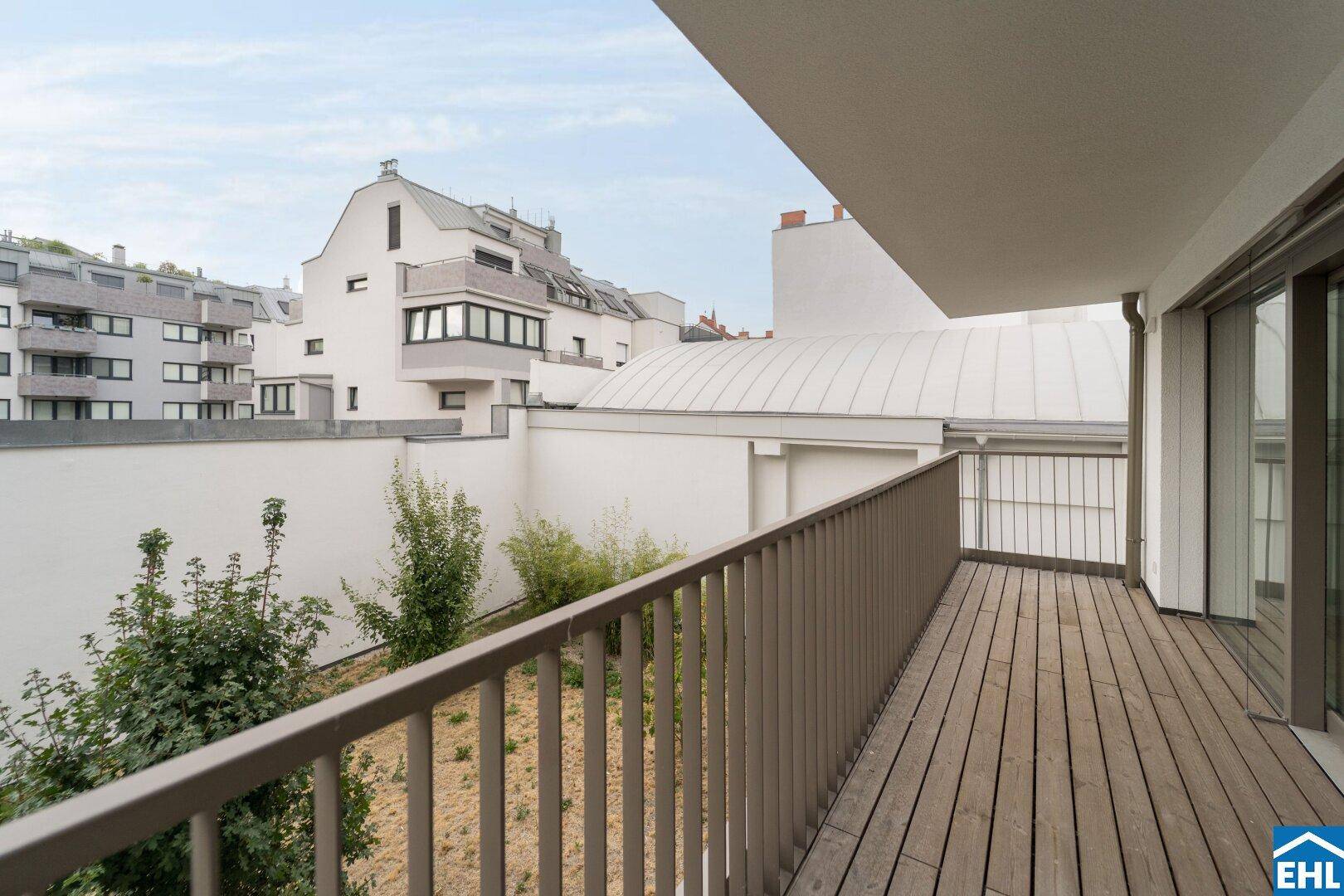 Langer Balkon mit Holzbelag und Blick auf die Nachbarschaft und einen kleinen Gartenbereich.