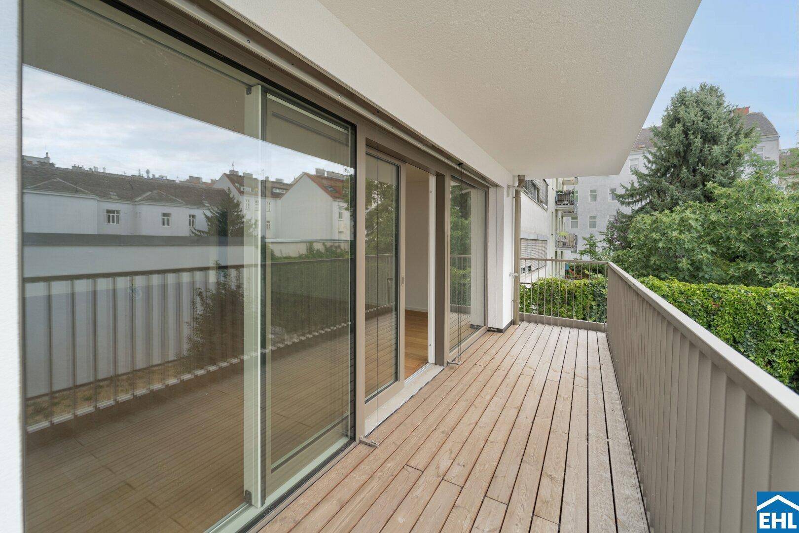 Breiter Balkon mit Holzfußboden und großen Schiebetüren, die viel Licht ins Innere lassen.