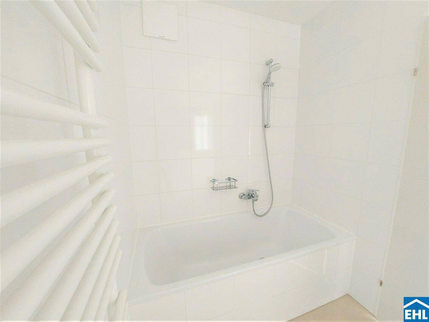 Modernes Badezimmer mit weißen Fliesen, Badewanne und beheiztem Handtuchhalter.
