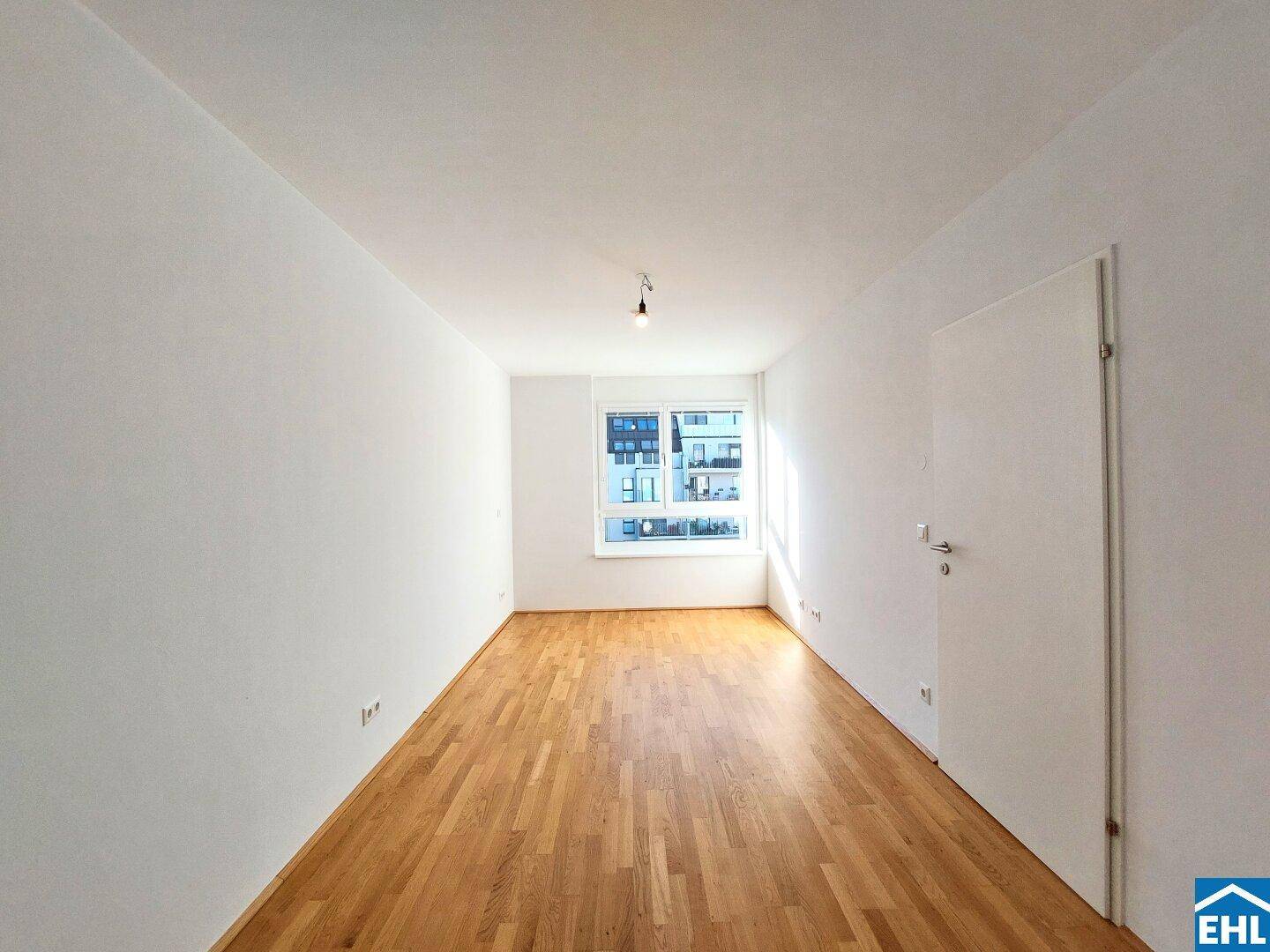 Helles Zimmer mit Parkettboden und einem Fenster, das viel Tageslicht hereinlässt.