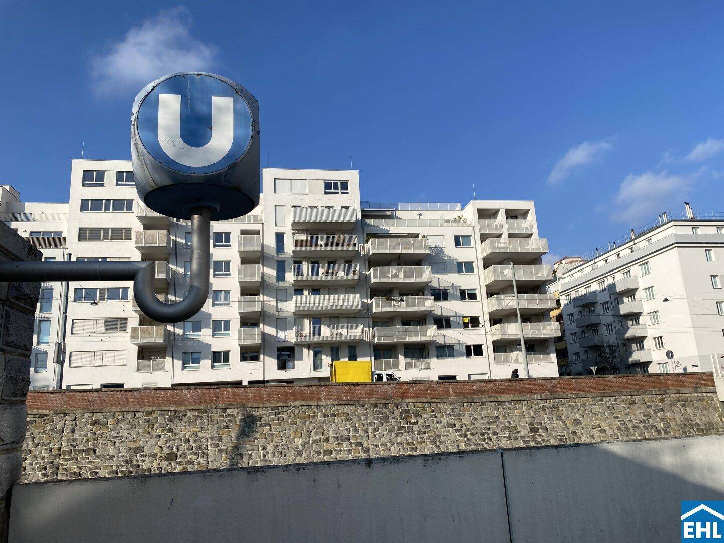 U-Bahn-Station im Vordergrund mit modernen Wohngebäuden im Hintergrund unter blauem Himmel.