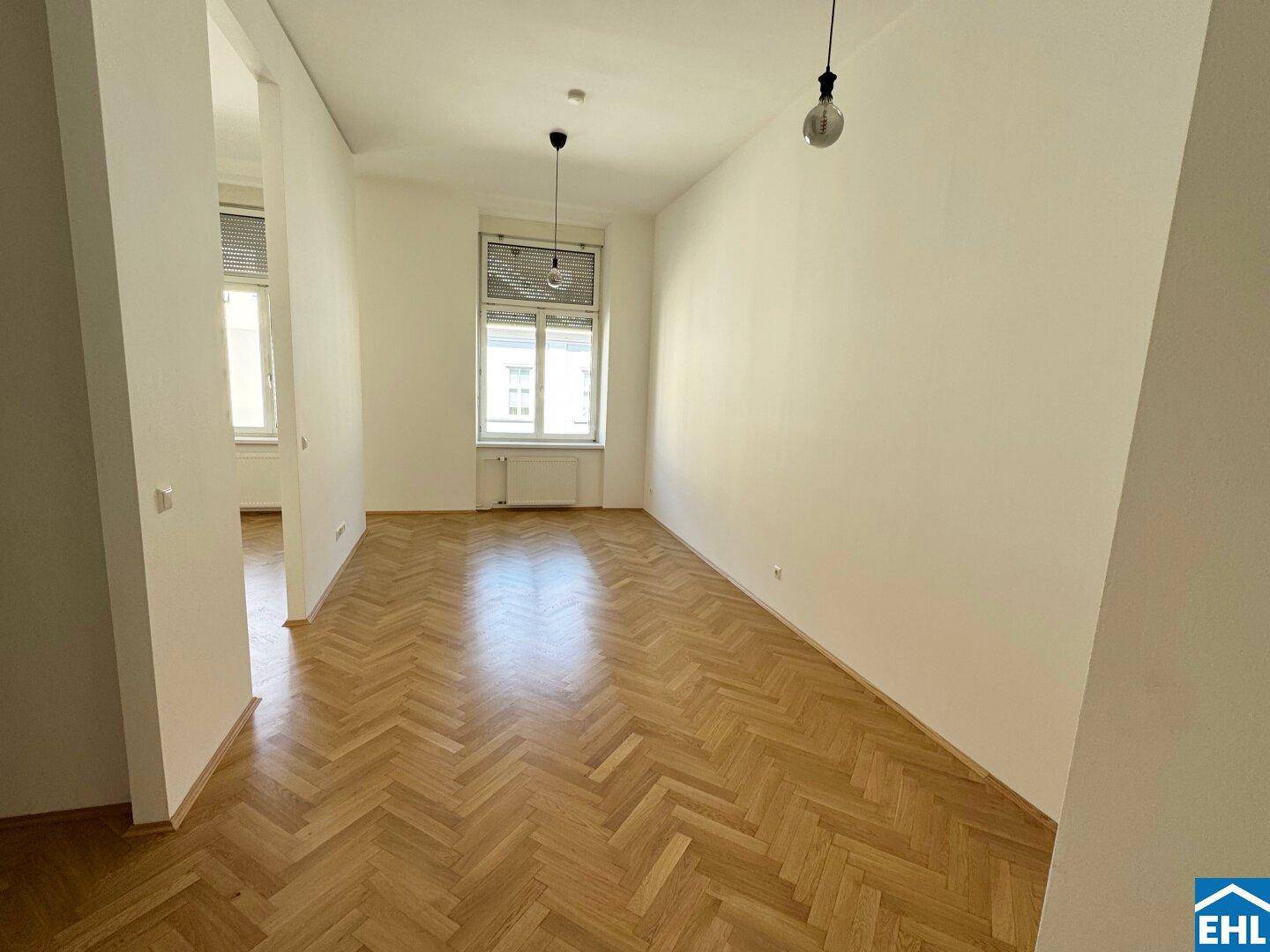 Heller Wohnraum mit Fischgrätparkettboden und großen Fenstern, die viel Tageslicht hereinlassen.