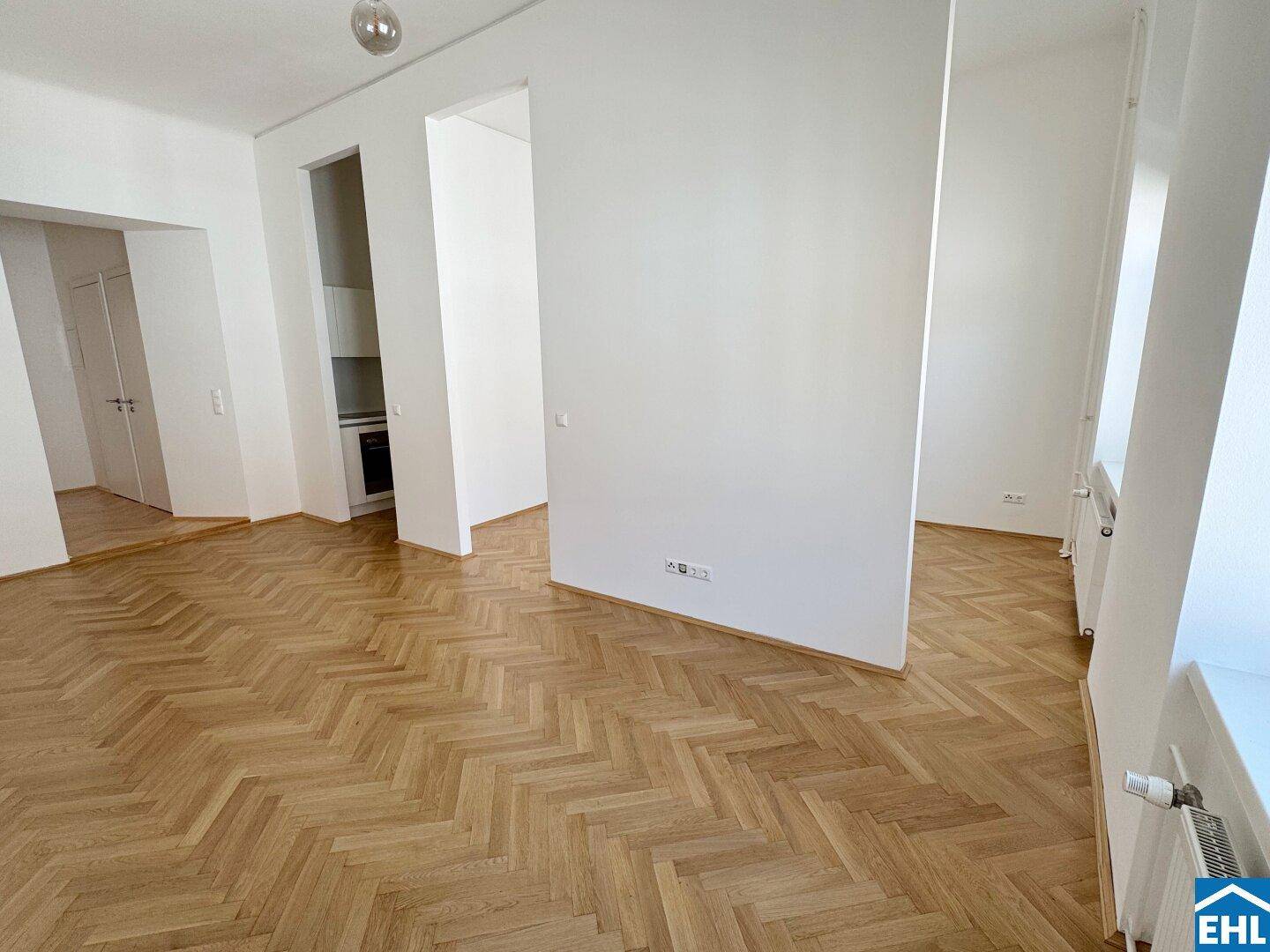 Geräumiger, leerer Raum mit elegantem Fischgrätparkett und weißen Wänden, der viel Gestaltungspotenzial bietet.