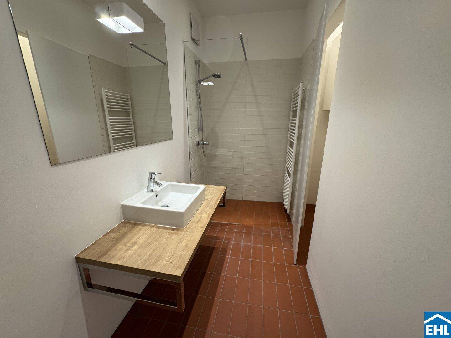 Modernes Badezimmer mit ebenerdiger Dusche, Einzelwaschbecken und Terrakotta-Fliesenboden.