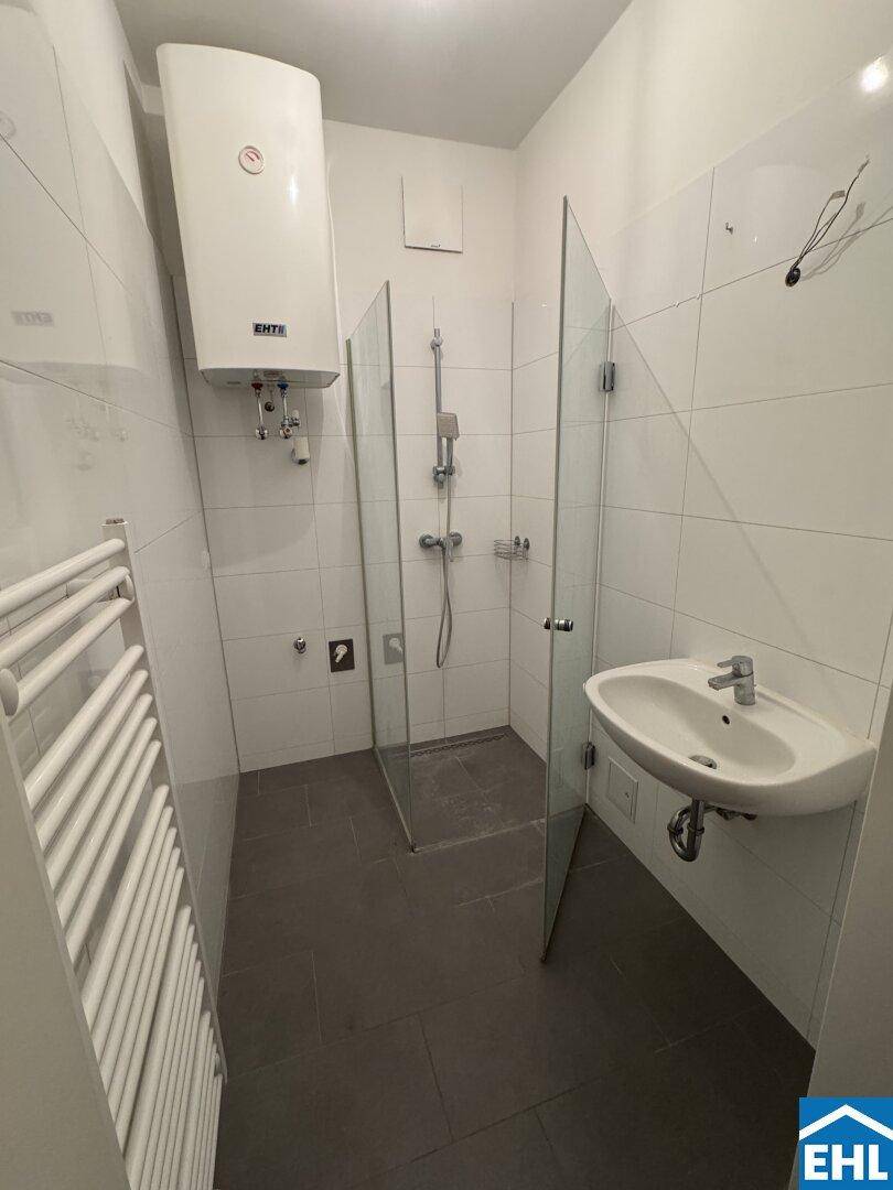 Modernes Badezimmer mit weißen Fliesen, ebenerdiger Dusche, Waschbecken und beheiztem Handtuchhalter.