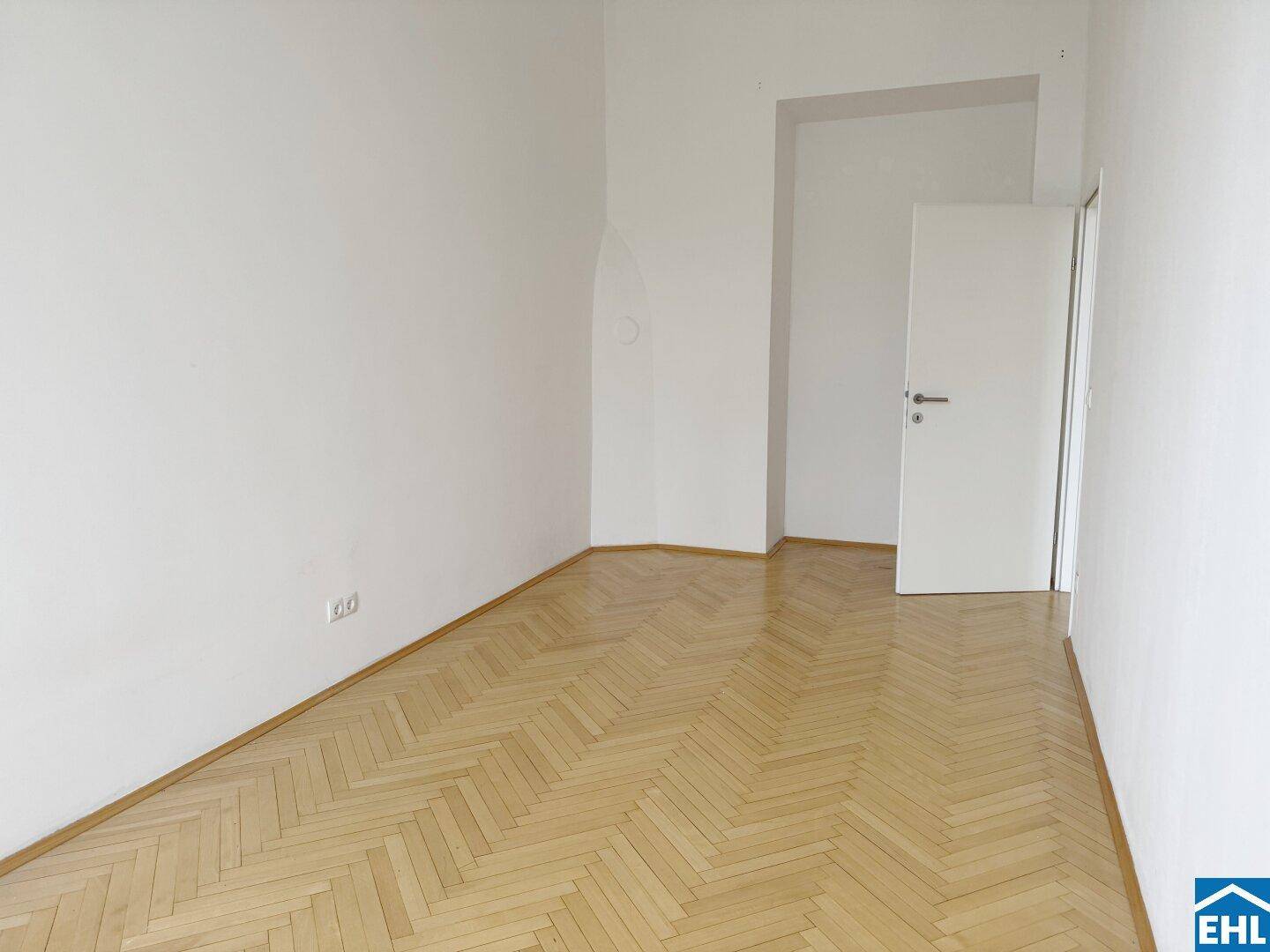 Leeres Zimmer mit hellem Fischgrätparkett und weiß gestrichenen Wänden, bereit zur individuellen Gestaltung.