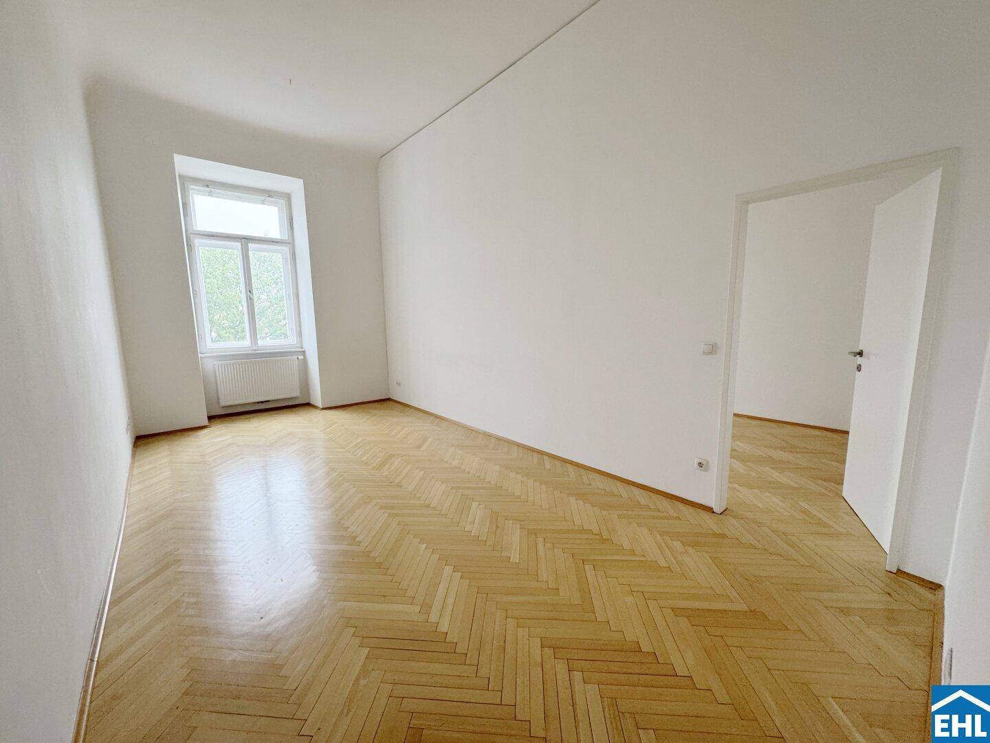 Geräumiges, helles Zimmer mit klassischem Fischgrätparkett und einem großen Fenster, das den Raum erhellt.