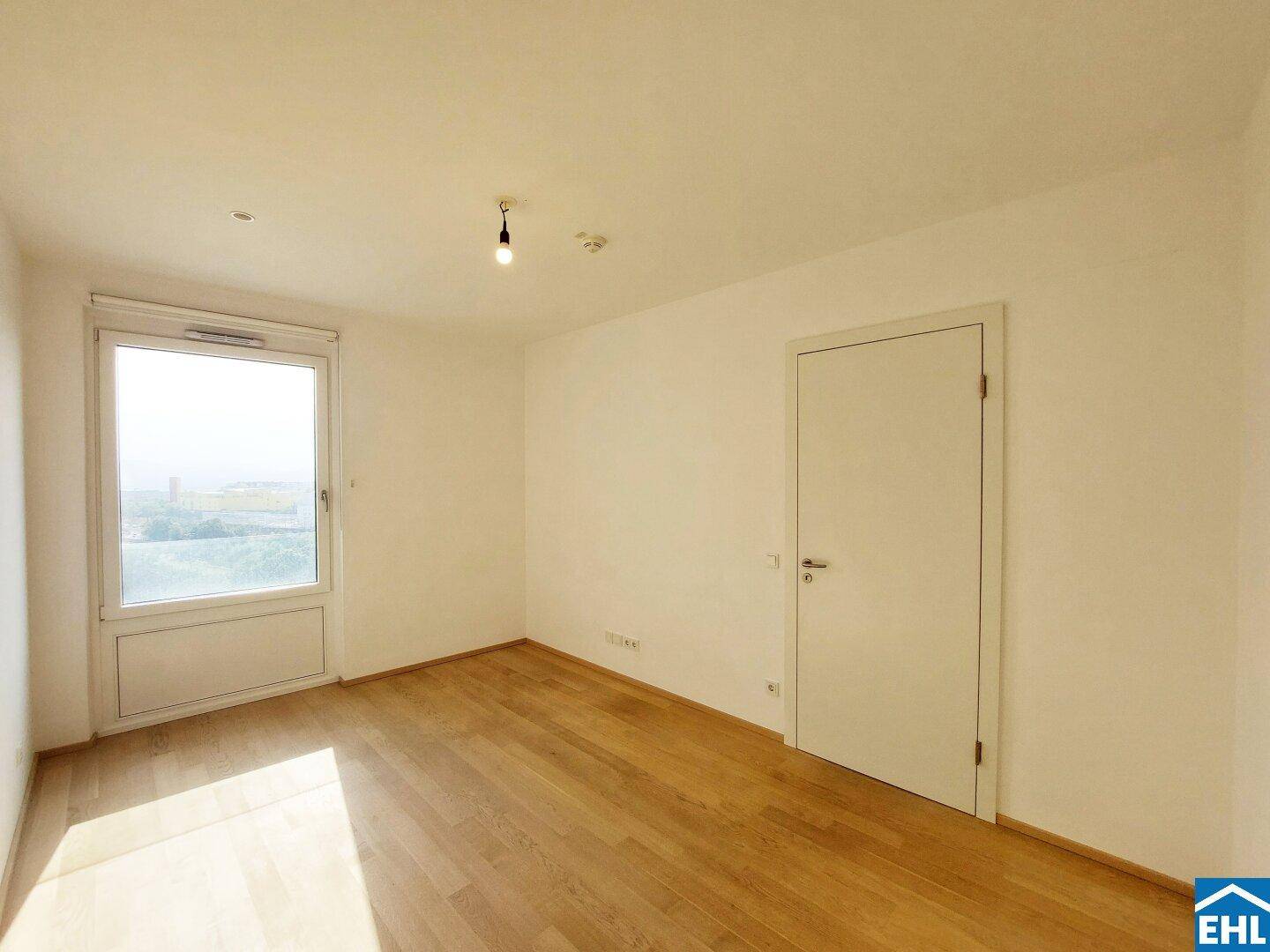 Helles Schlafzimmer mit Holzboden und einem Fenster, das viel Tageslicht hereinlässt.