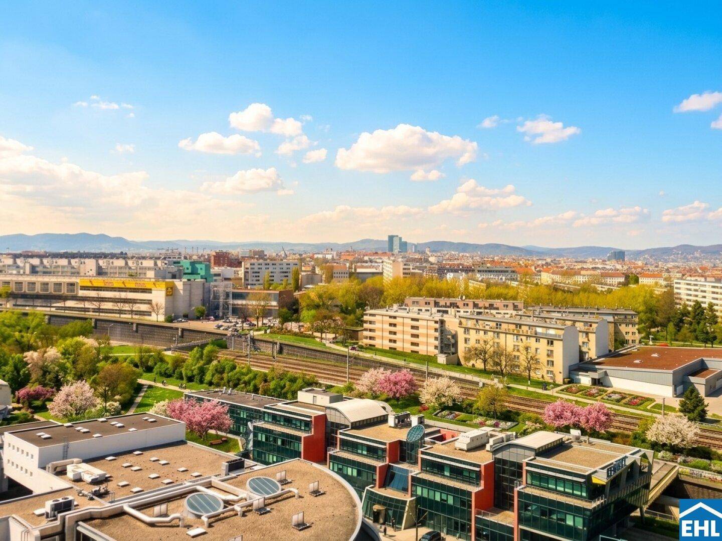 Panoramablick über die Stadt mit grünen Flächen und Gebäuden unter blauem Himmel.
