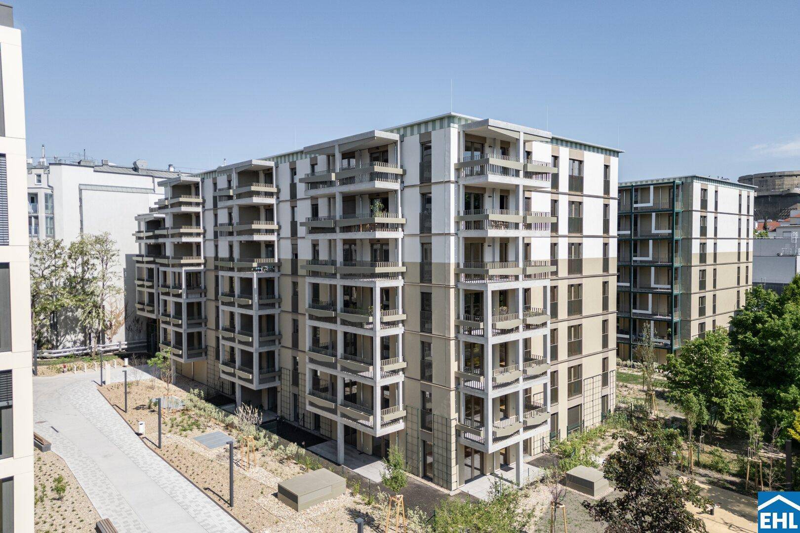 Moderner Wohnkomplex mit mehreren Gebäuden und Balkonen unter blauem Himmel, umgeben von Grünflächen.