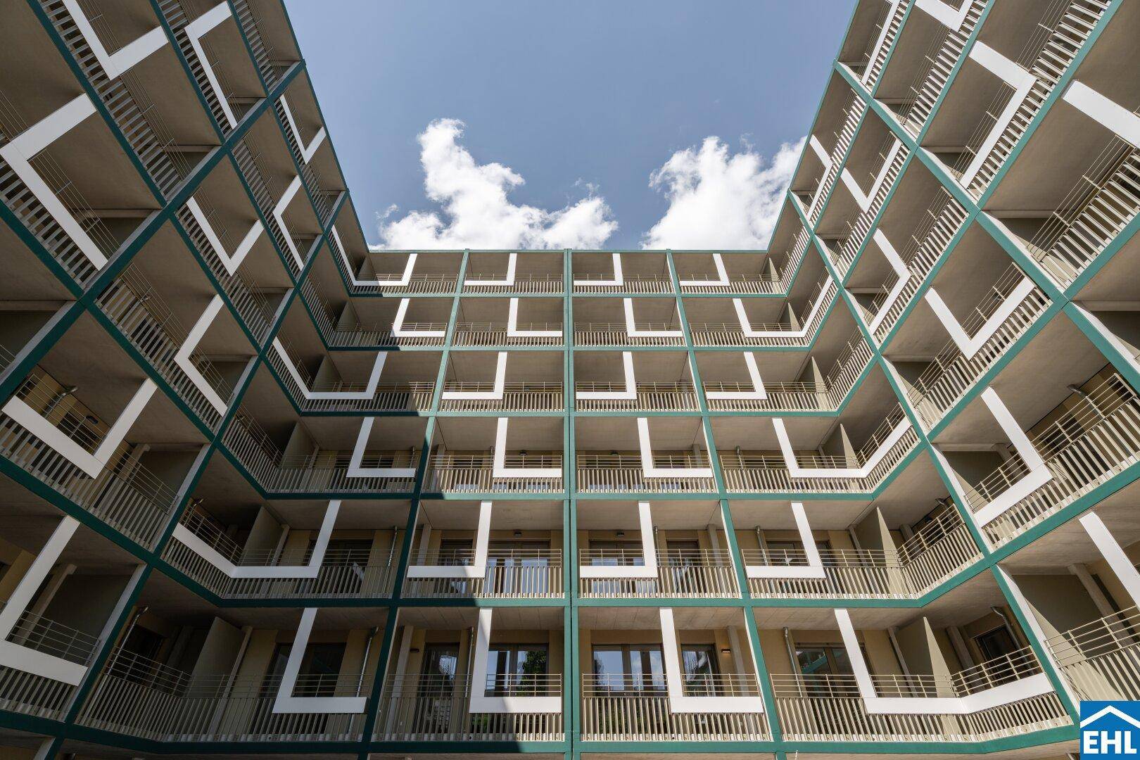 Innenhofansicht eines modernen Wohnkomplexes mit vielen Balkonen und offener Architektur.