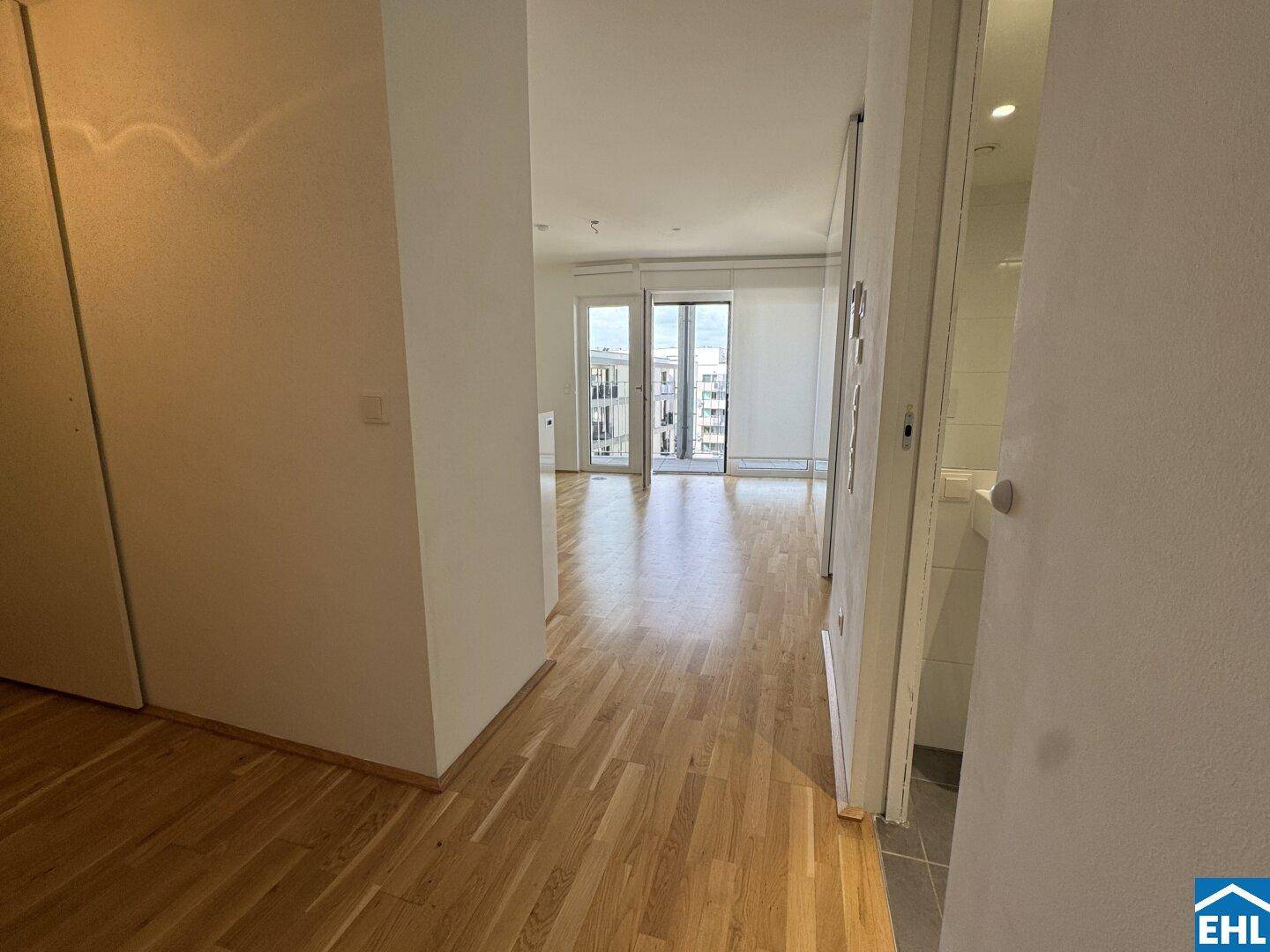 Heller Flur mit Parkettboden, der in den offenen Wohnbereich mit Balkonzugang führt.
