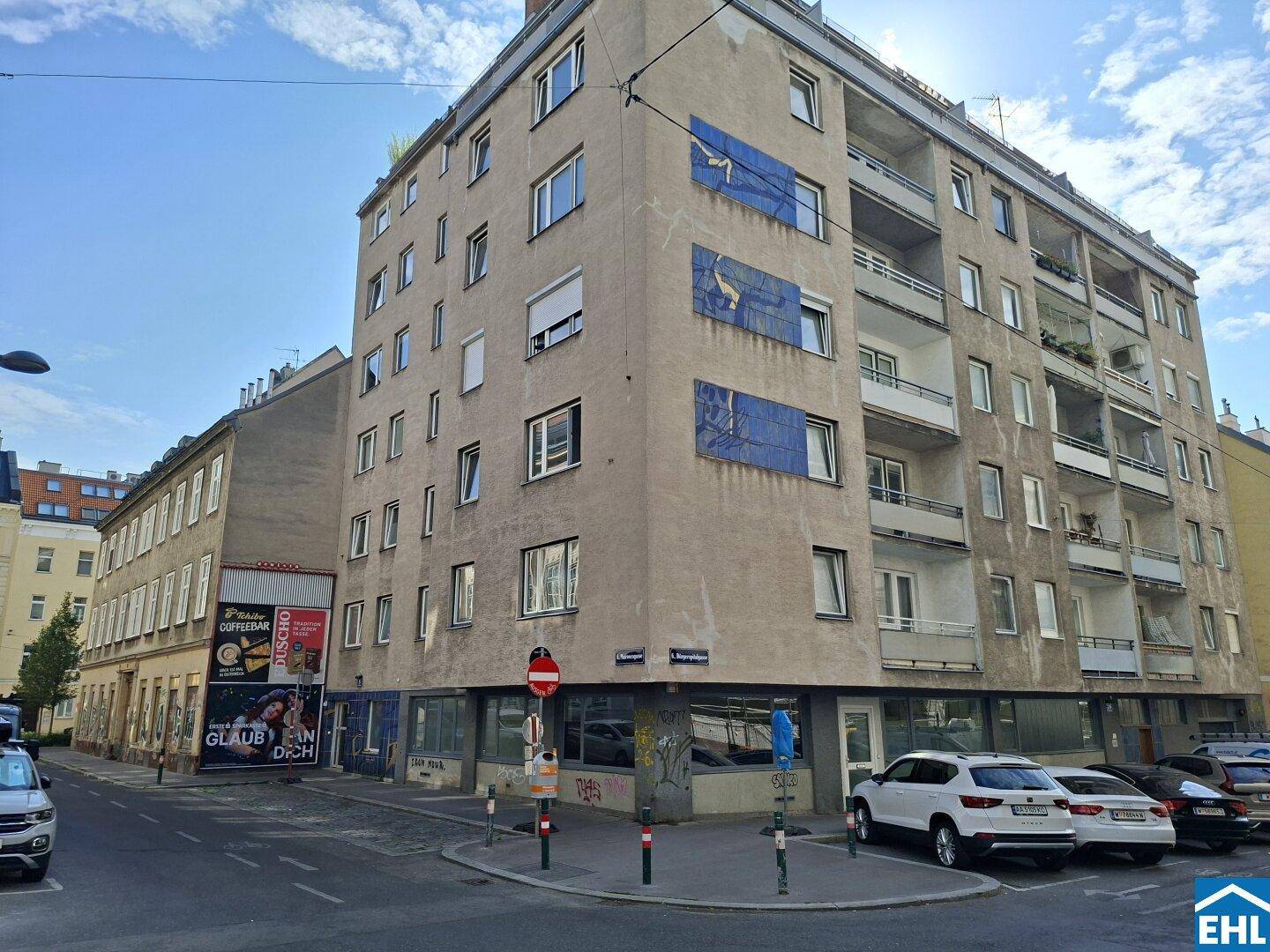 Mehrstöckiges Wohngebäude an einer Straßenecke mit parkenden Autos.