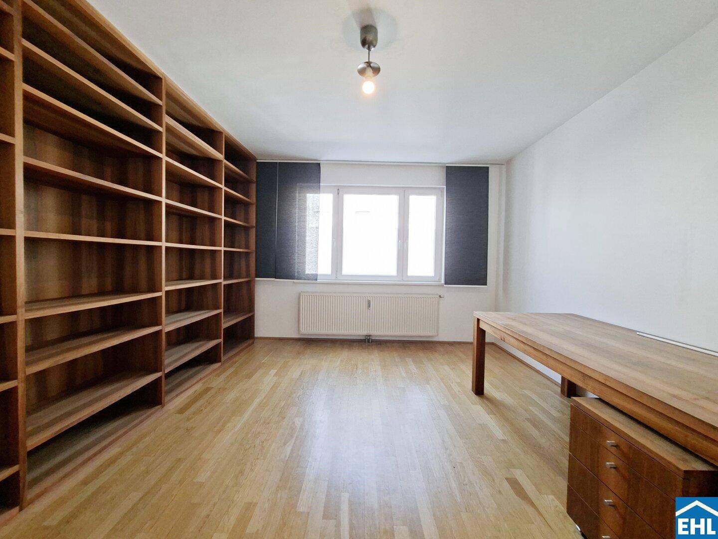 Geräumiges Zimmer mit großer Bücherwand, Holztisch und Parkettboden.