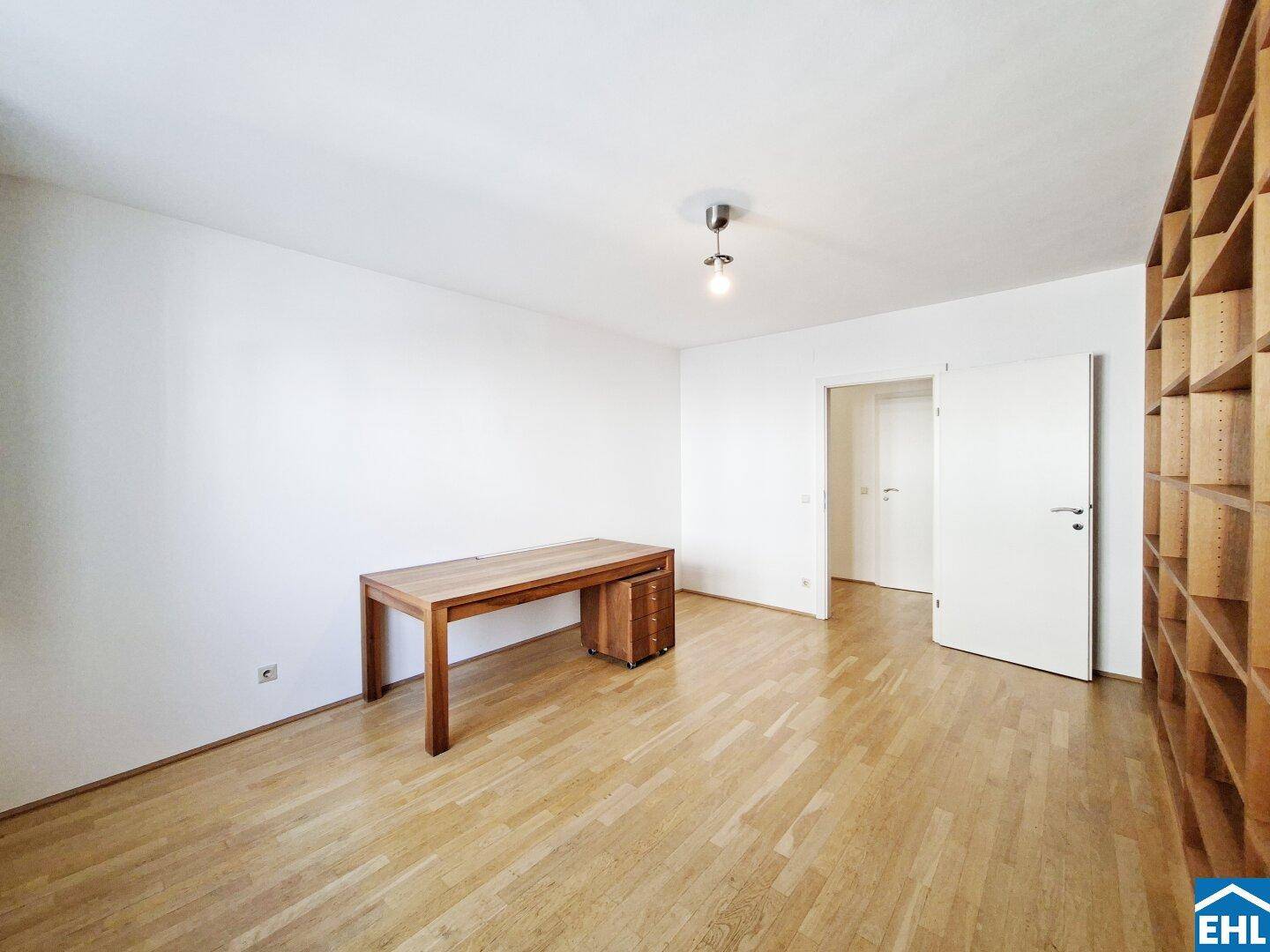 Helles Arbeitszimmer mit Holztisch, Parkettboden und Zugang zu weiteren Räumen.
