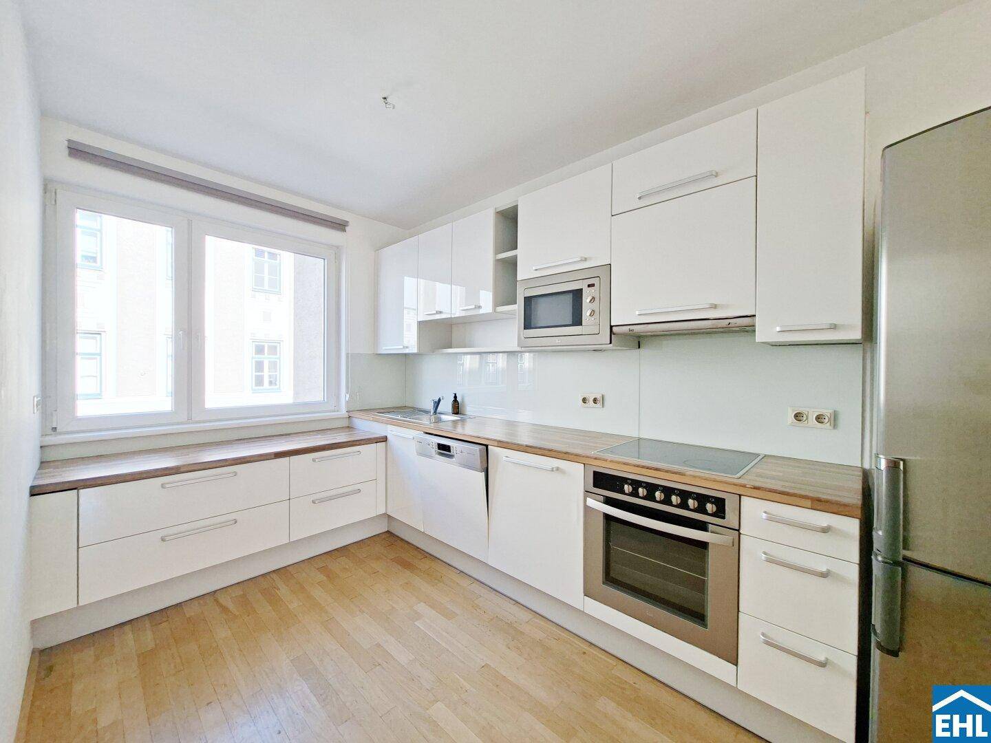 Moderne Einbauküche mit weißen Schränken, Holzarbeitsplatte und Fenster.