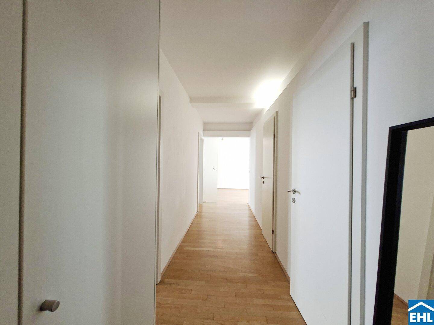 Schmaler Flur mit Holzboden und weißen Türen, der zu weiteren Räumen führt.
