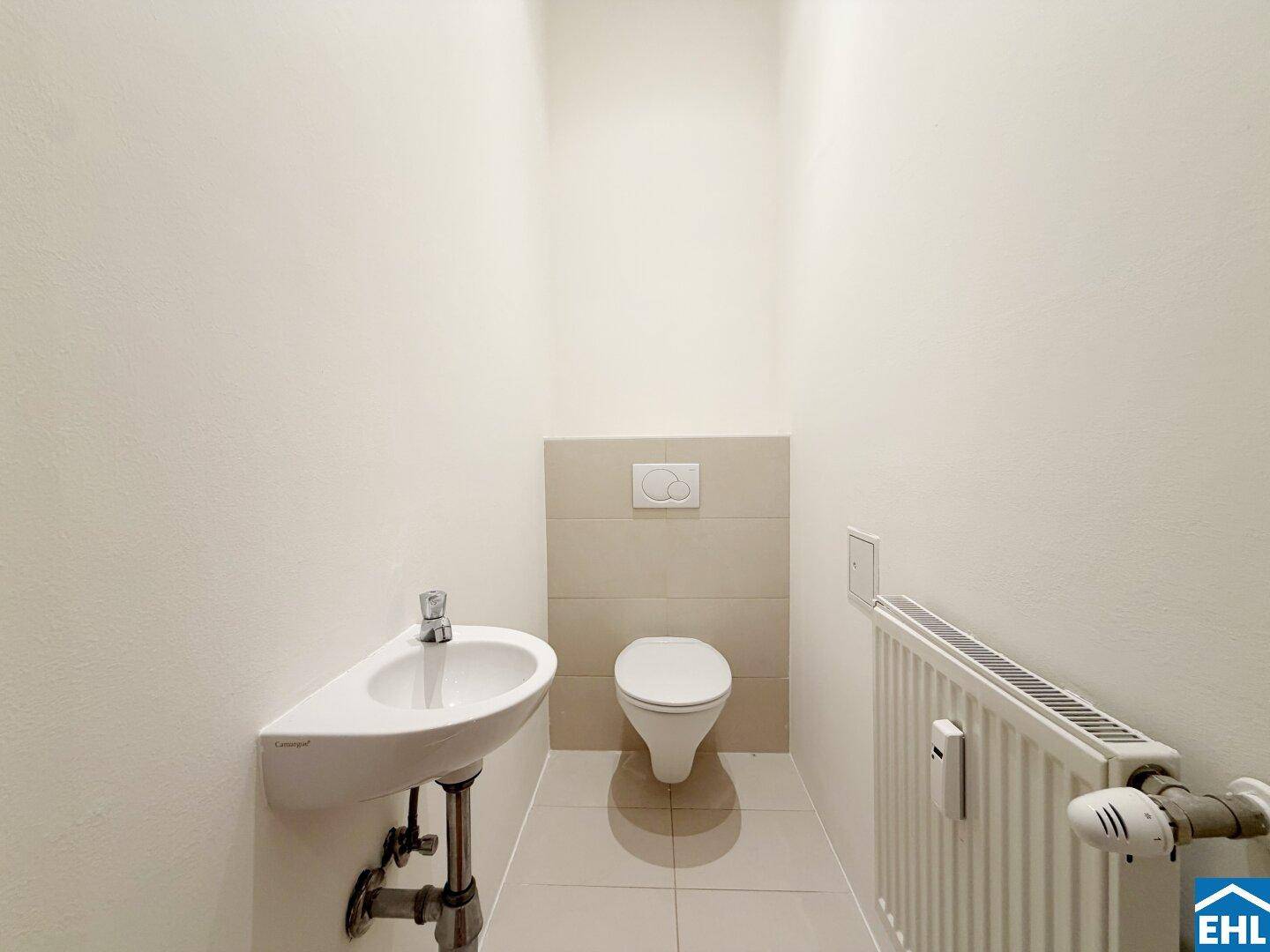 Kleines Gäste-WC mit wandhängendem WC, Eckwaschbecken und Heizkörper.