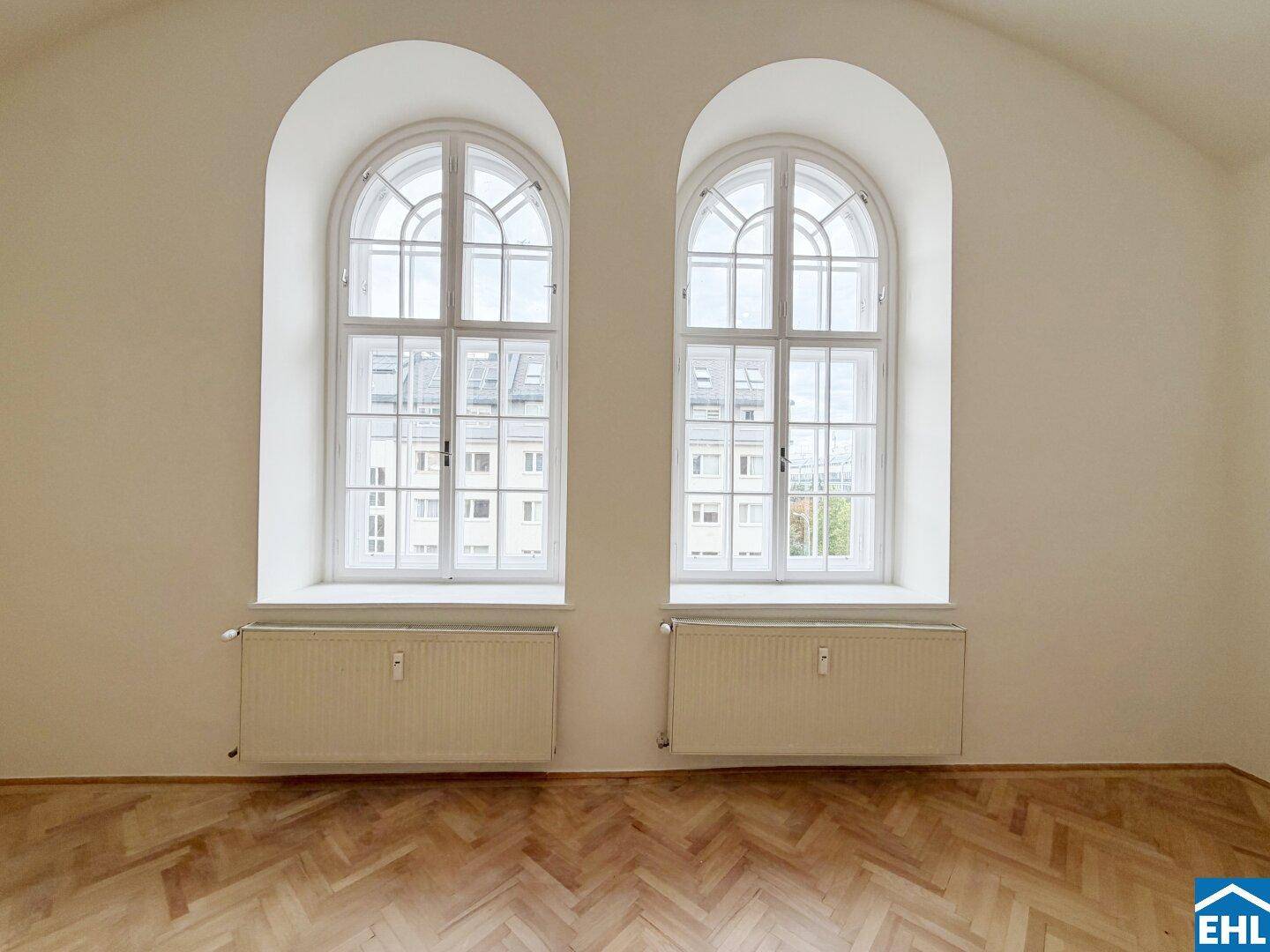 Zwei große, elegante Rundbogenfenster mit Heizkörpern darunter und Blick auf die Stadt.