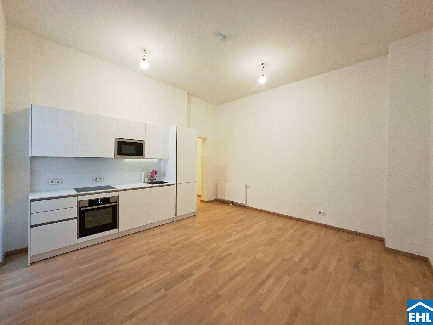 Geräumiger Wohnbereich mit integrierter Küchenzeile und hellem Parkettboden, bietet vielseitige Gestaltungsmöglichkeiten.