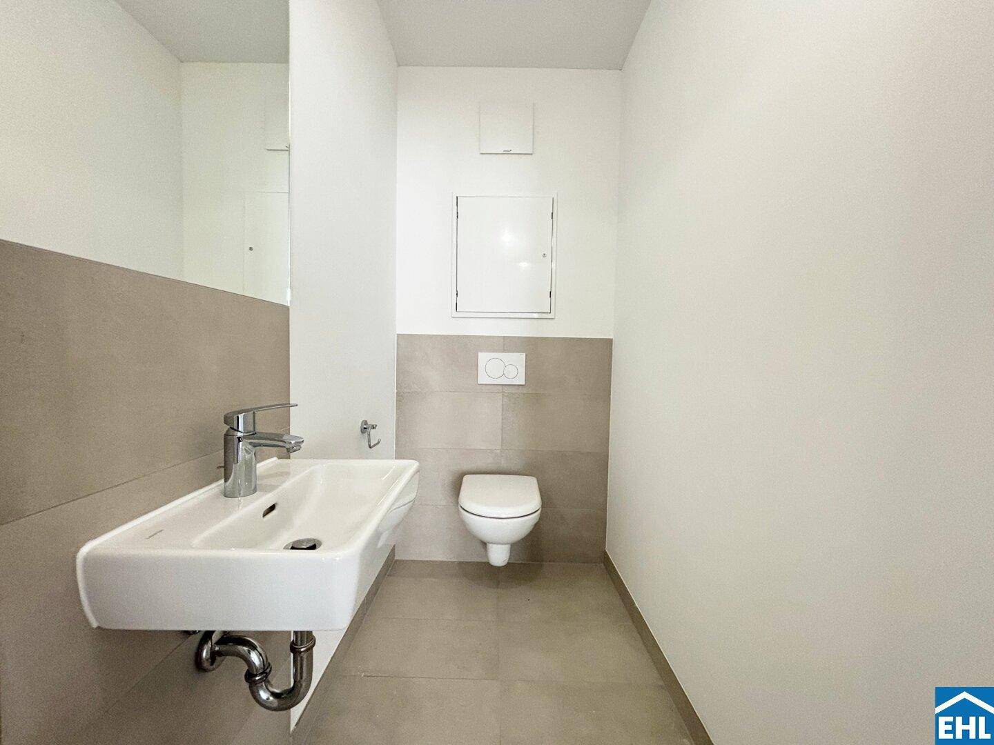 Modernes Gäste-WC mit Wandwaschbecken und Wand-WC, hell gefliest.