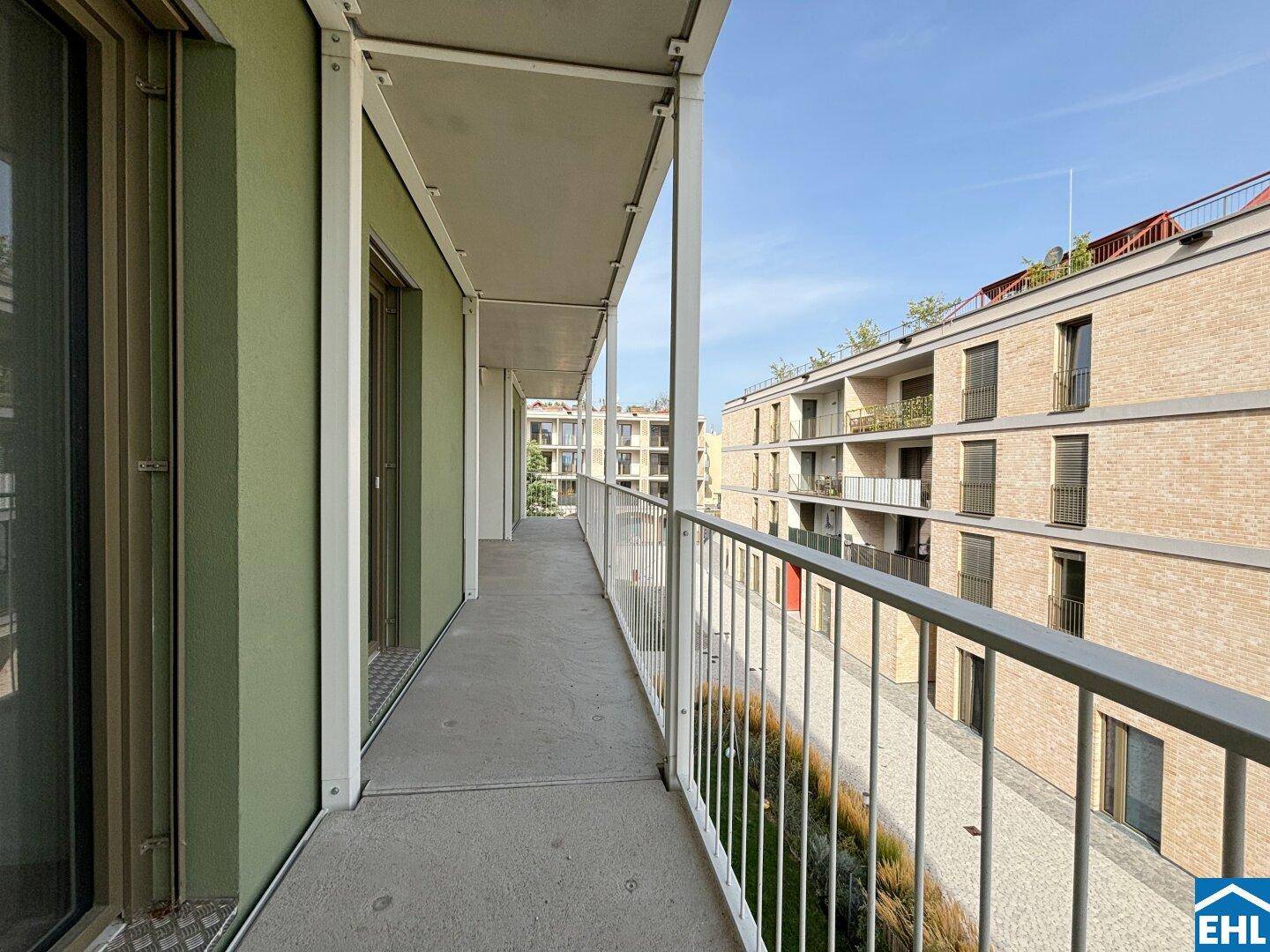 Langer Balkon mit Blick auf die moderne Wohnanlage und viel Tageslicht.