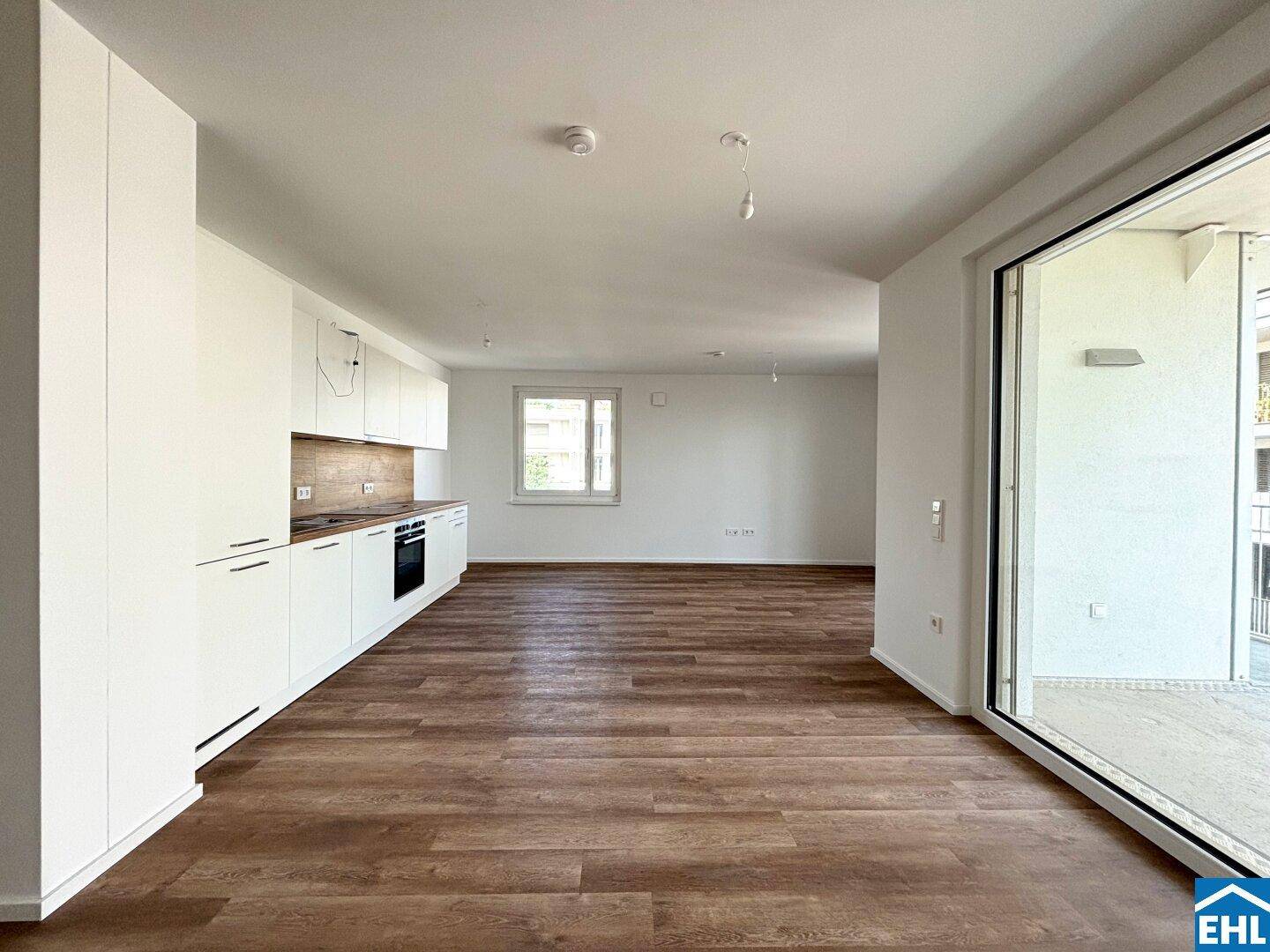 Moderner Wohn- und Essbereich mit Einbauküche und Zugang zum Balkon.