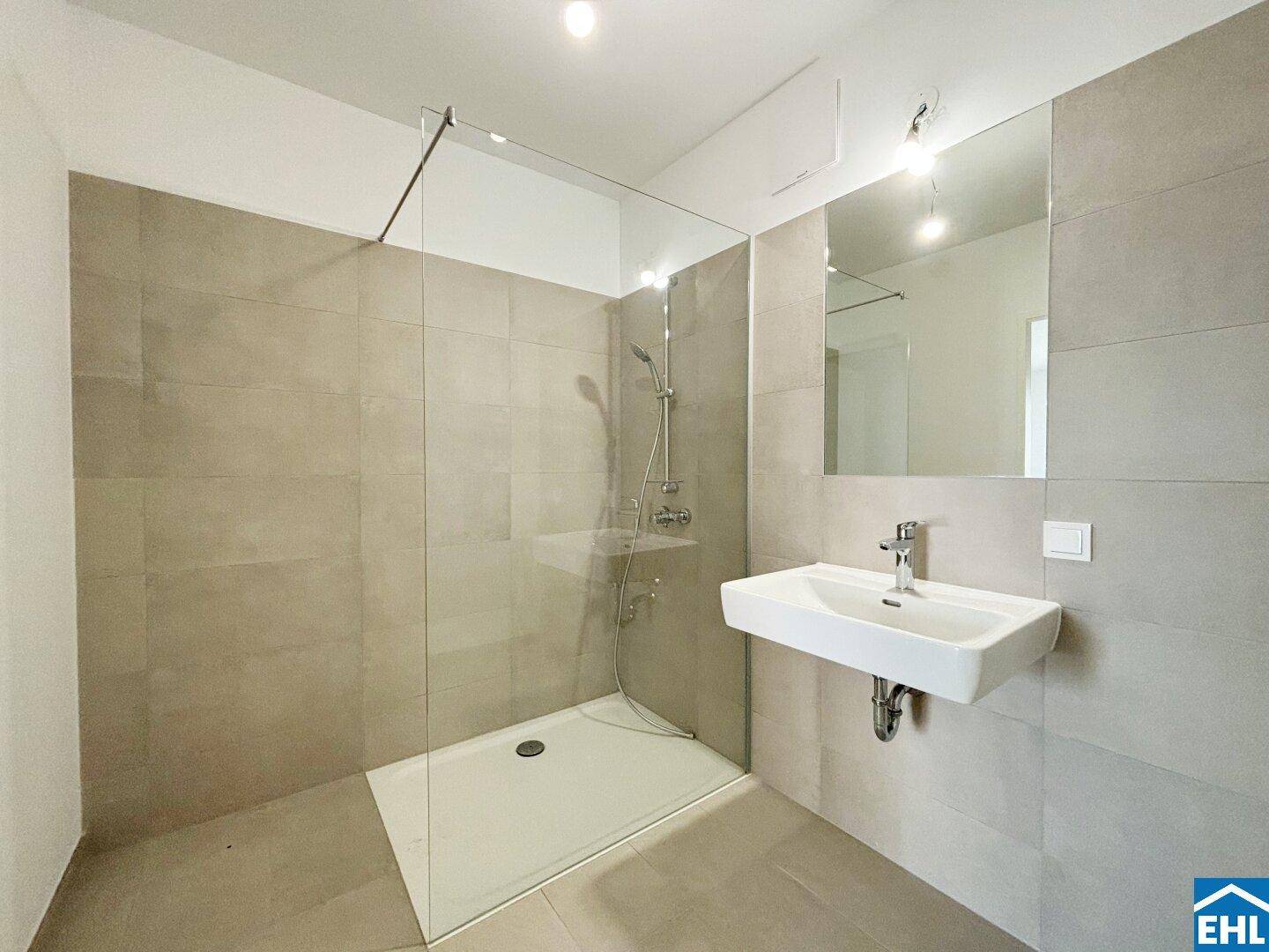 Modernes Badezimmer mit ebenerdiger Dusche, Wandwaschbecken und großen Fliesen.