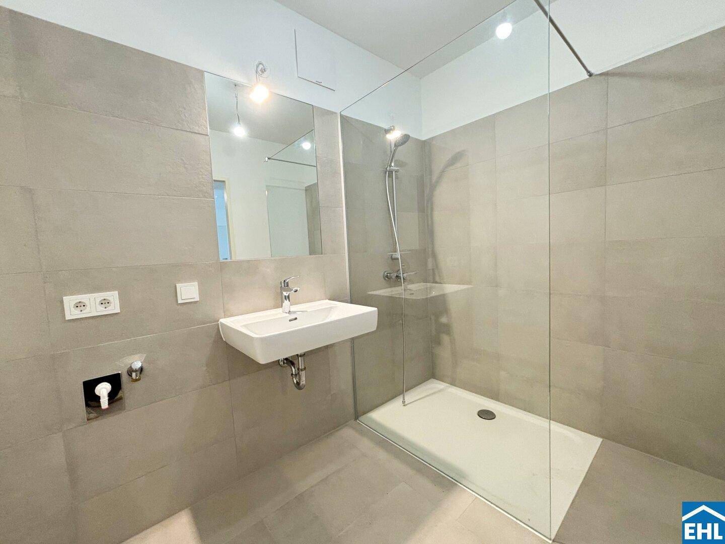 Modernes Badezimmer mit ebenerdiger Dusche, Wandwaschbecken und grauen Fliesen.
