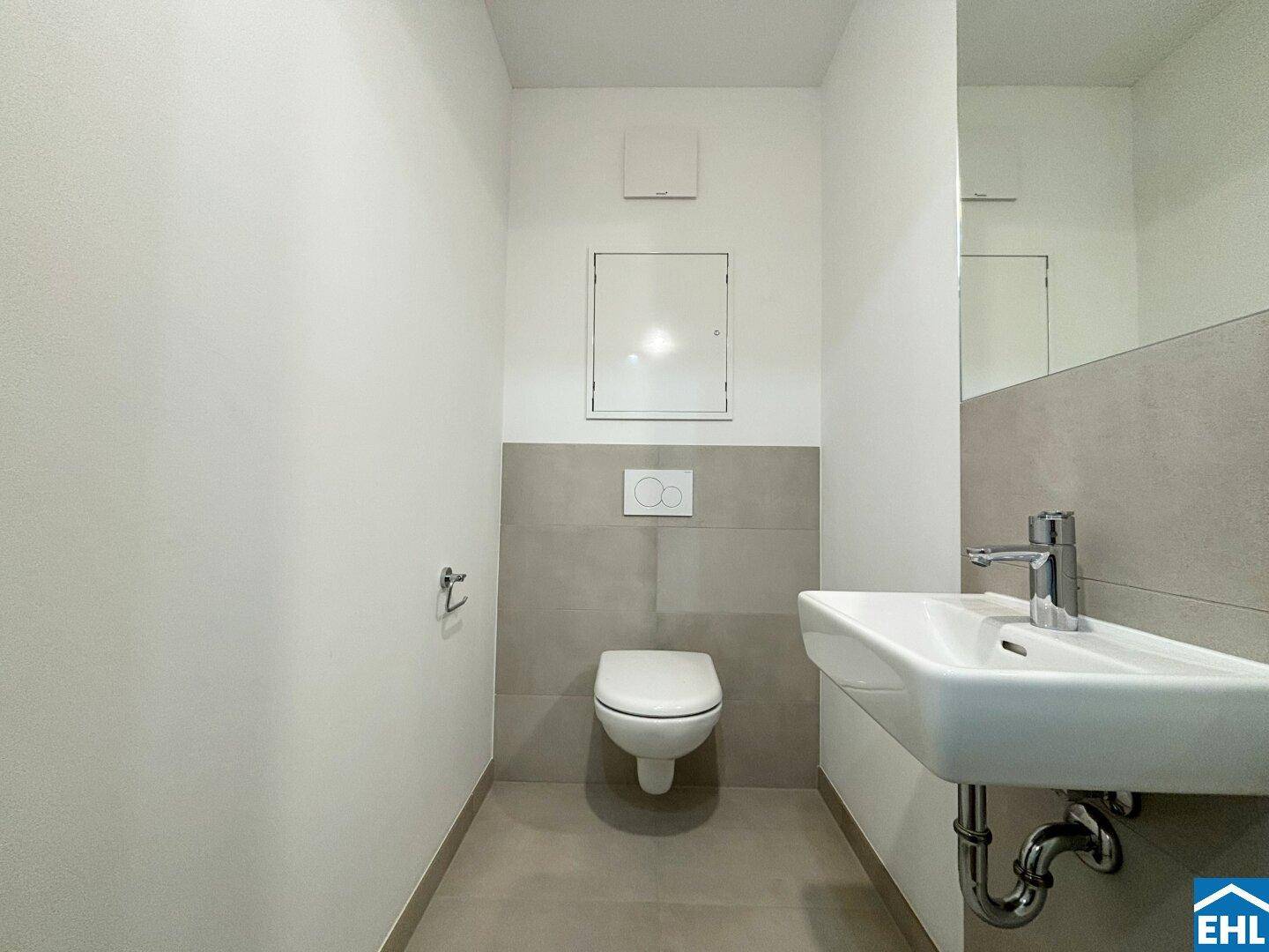 Separates WC mit wandhängender Toilette, Waschbecken und modernen Fliesen.