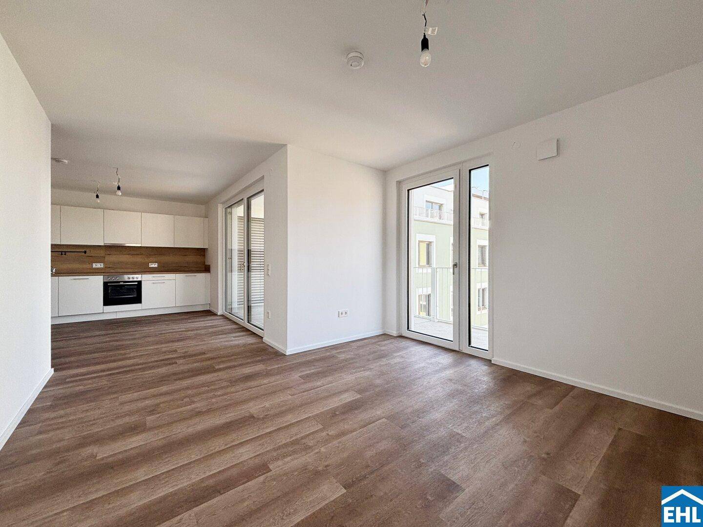 Offener Wohnbereich mit moderner Einbauküche, Laminatboden und Zugang zum Balkon.