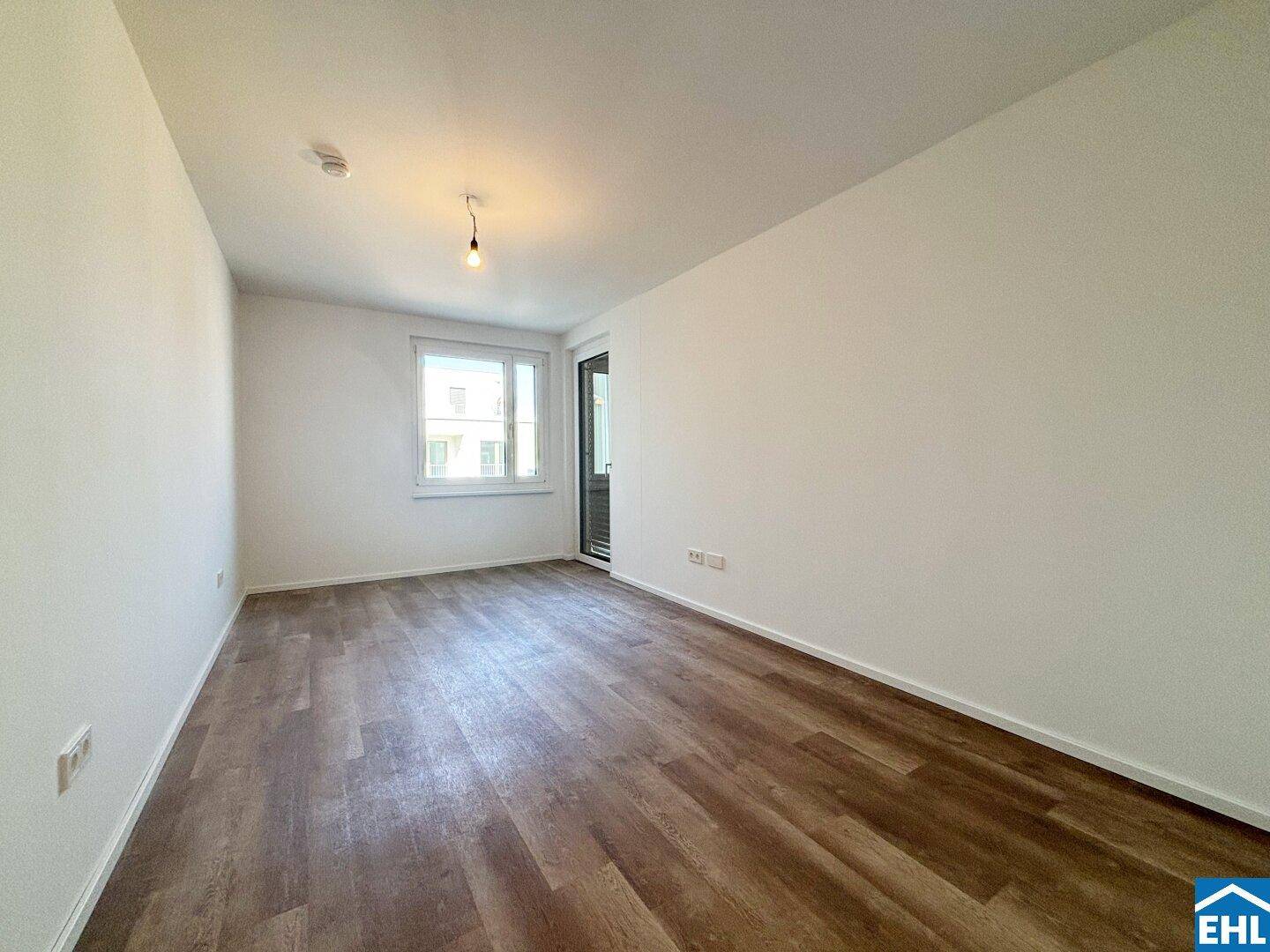 Helles Schlafzimmer mit Laminatboden, weißen Wänden und Zugang zu einem kleinen Außenbereich.