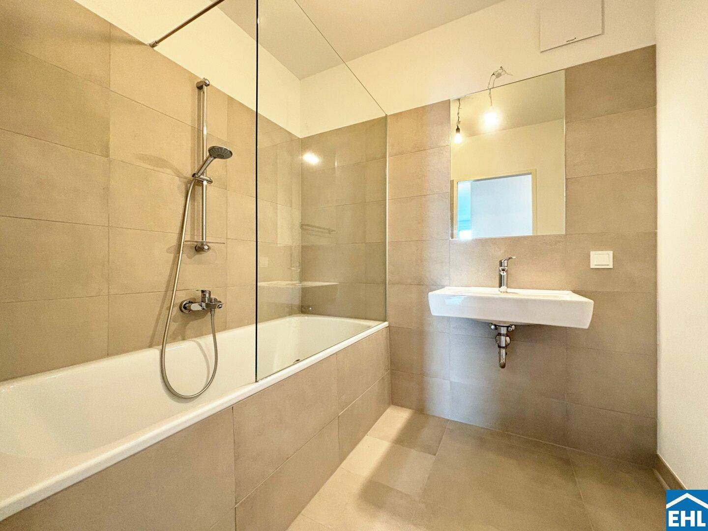Helles Badezimmer mit Badewanne, Einzelwaschbecken und beigefarbenen Wand- und Bodenfliesen.