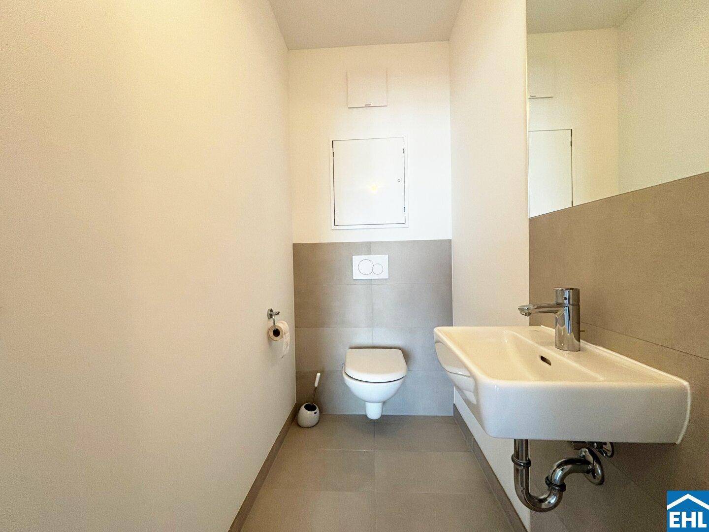 Praktisches Gäste-WC mit Einzelwaschbecken, Toilette und hellen Wandfliesen.
