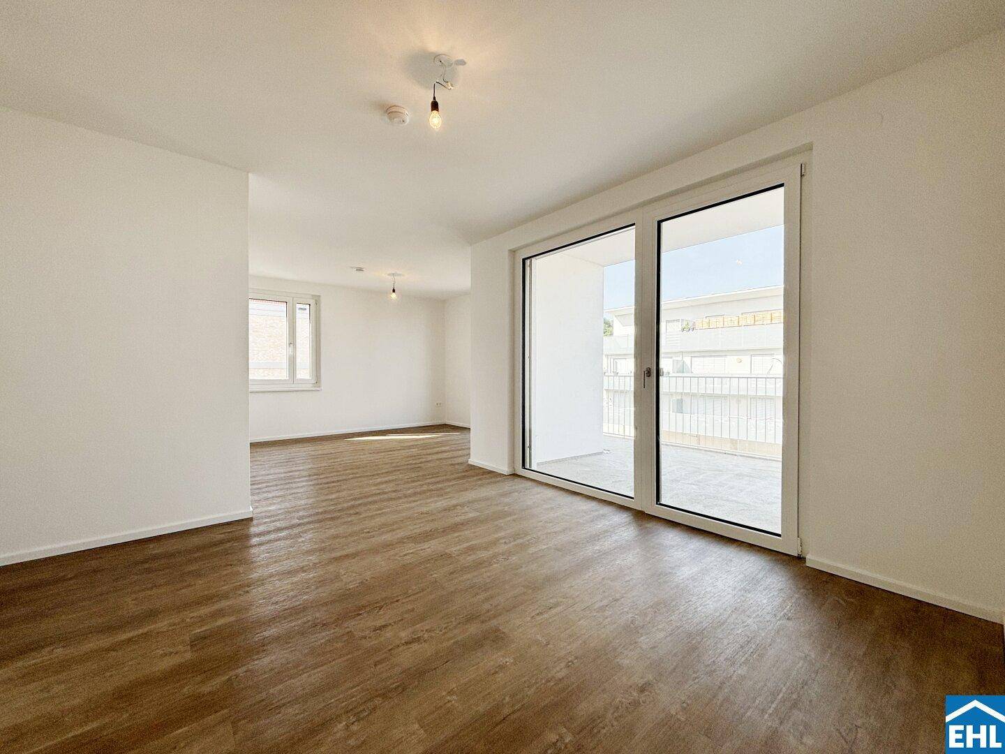 Geräumiges Wohnzimmer mit Laminatboden, großer Schiebetür zum Balkon und zusätzlichem Fenster.