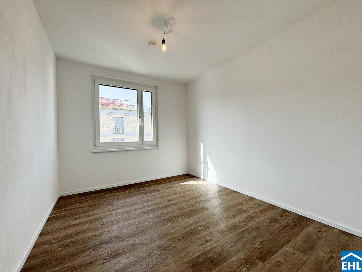 Helles Schlafzimmer mit Laminatboden und einem Fenster, das viel Tageslicht hereinlässt.