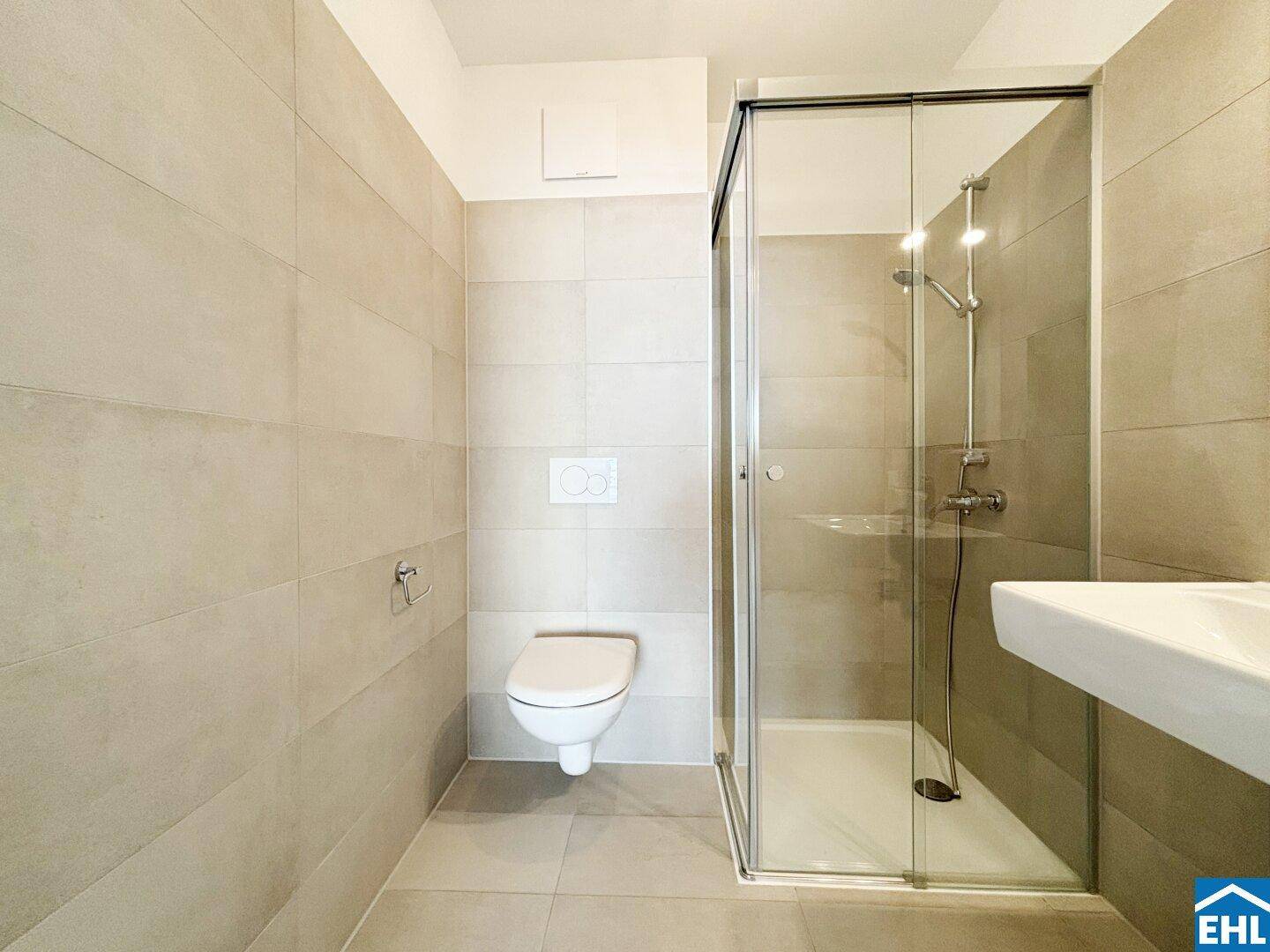 Modernes Badezimmer mit beigefarbenen Fliesen, wandhängendem WC und begehbarer Dusche.