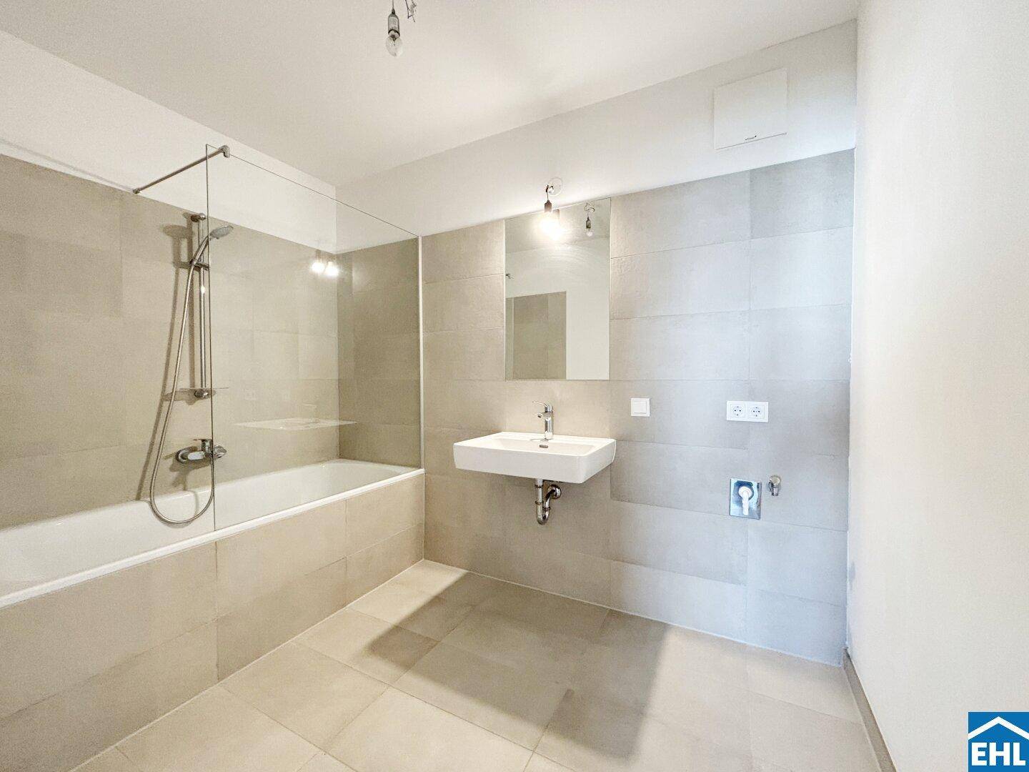 Helles Badezimmer mit Badewanne, Glasabtrennung und modernem Waschbecken.