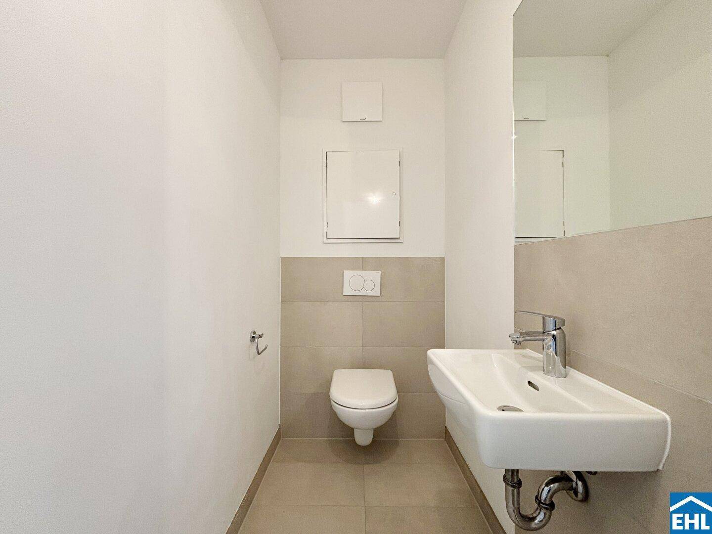Praktisches Gäste-WC mit wandhängendem WC, kleinem Waschbecken und beigefarbenen Fliesen.