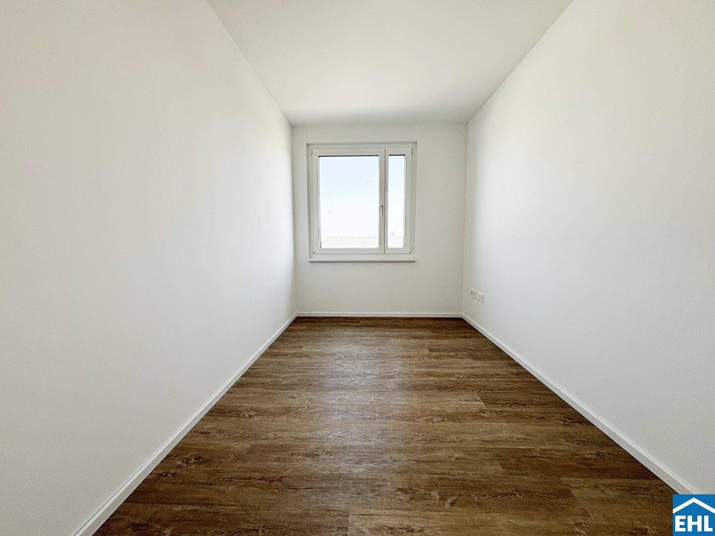 Ruhiges Schlafzimmer mit großem Fenster, Laminatboden und viel natürlichem Licht.