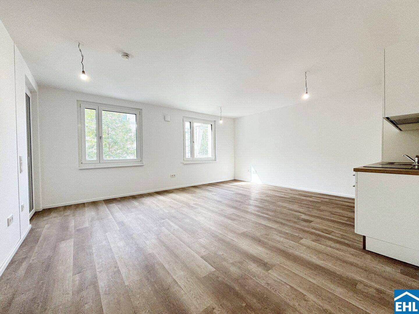 Lichtdurchfluteter Wohnbereich mit großen Fenstern und neuem Laminatboden.