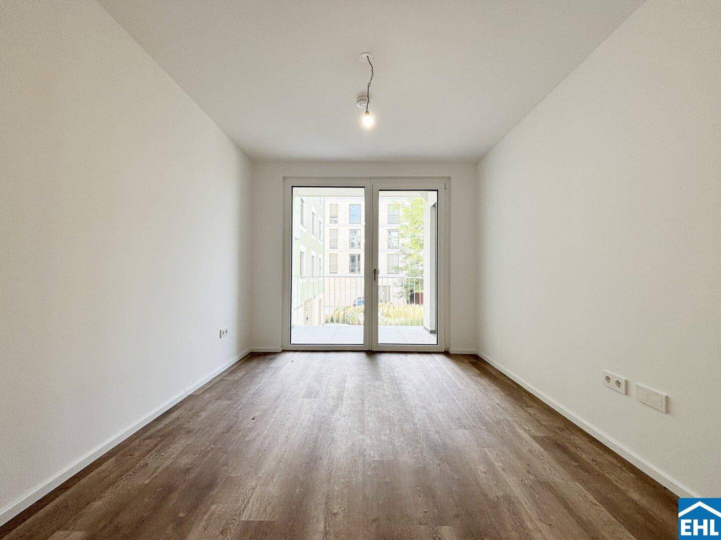 Leeres Zimmer mit Zugang zum Balkon und hellem Laminatboden.