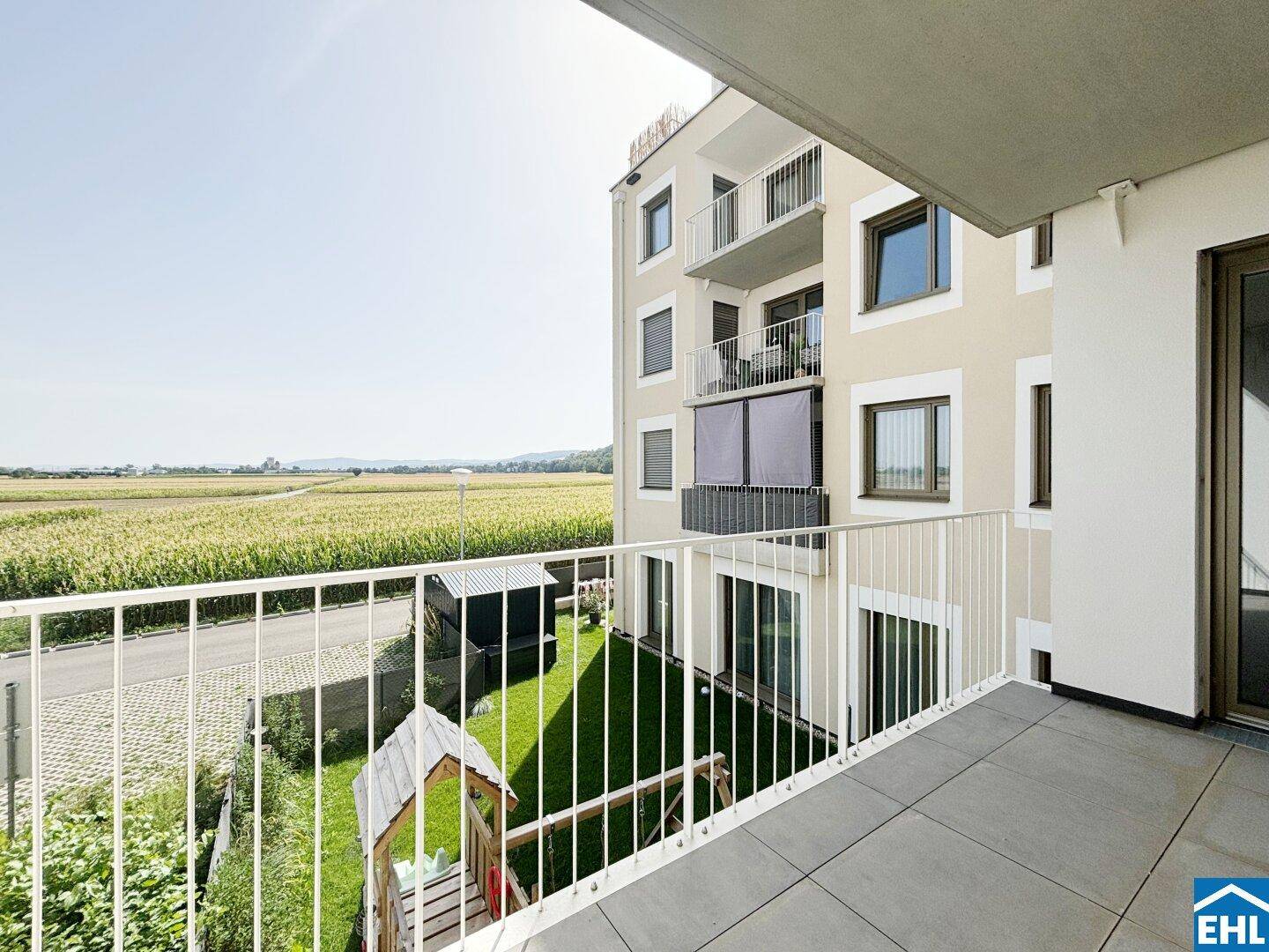 Balkon mit Blick auf das moderne Gebäude und die umliegenden Felder und Natur.