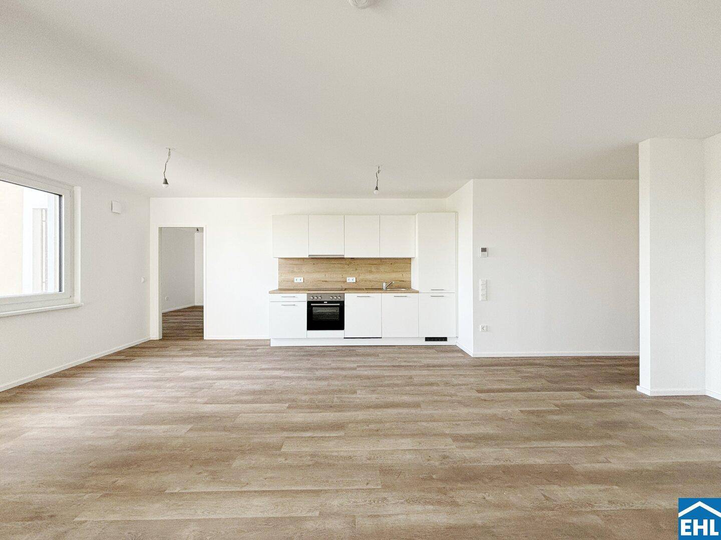 Heller offener Wohnbereich mit integrierter Küche und modernem Laminatboden in Holzoptik.