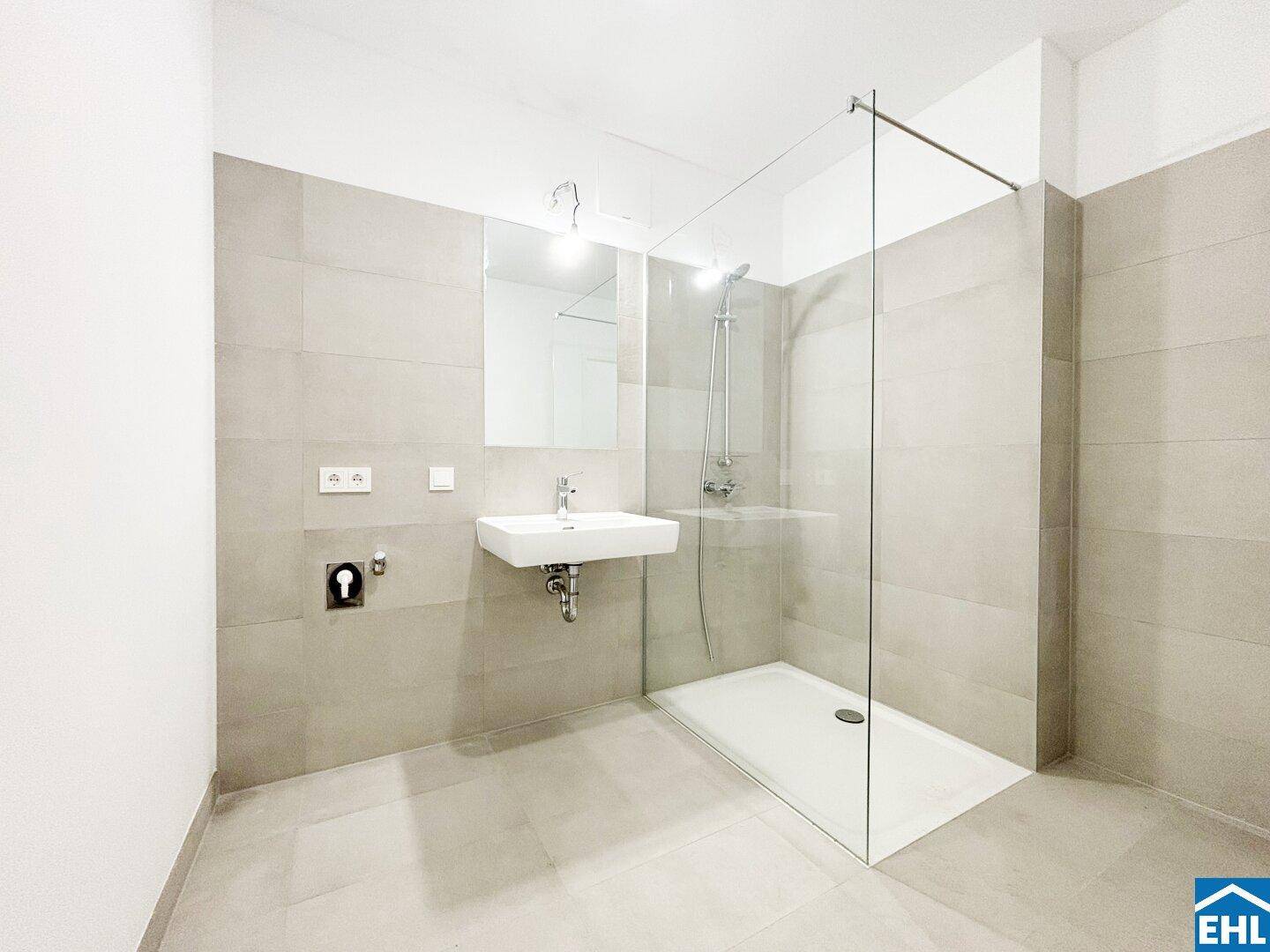 Modernes Badezimmer mit begehbarer Dusche, Waschbecken und hellen, großformatigen Fliesen.