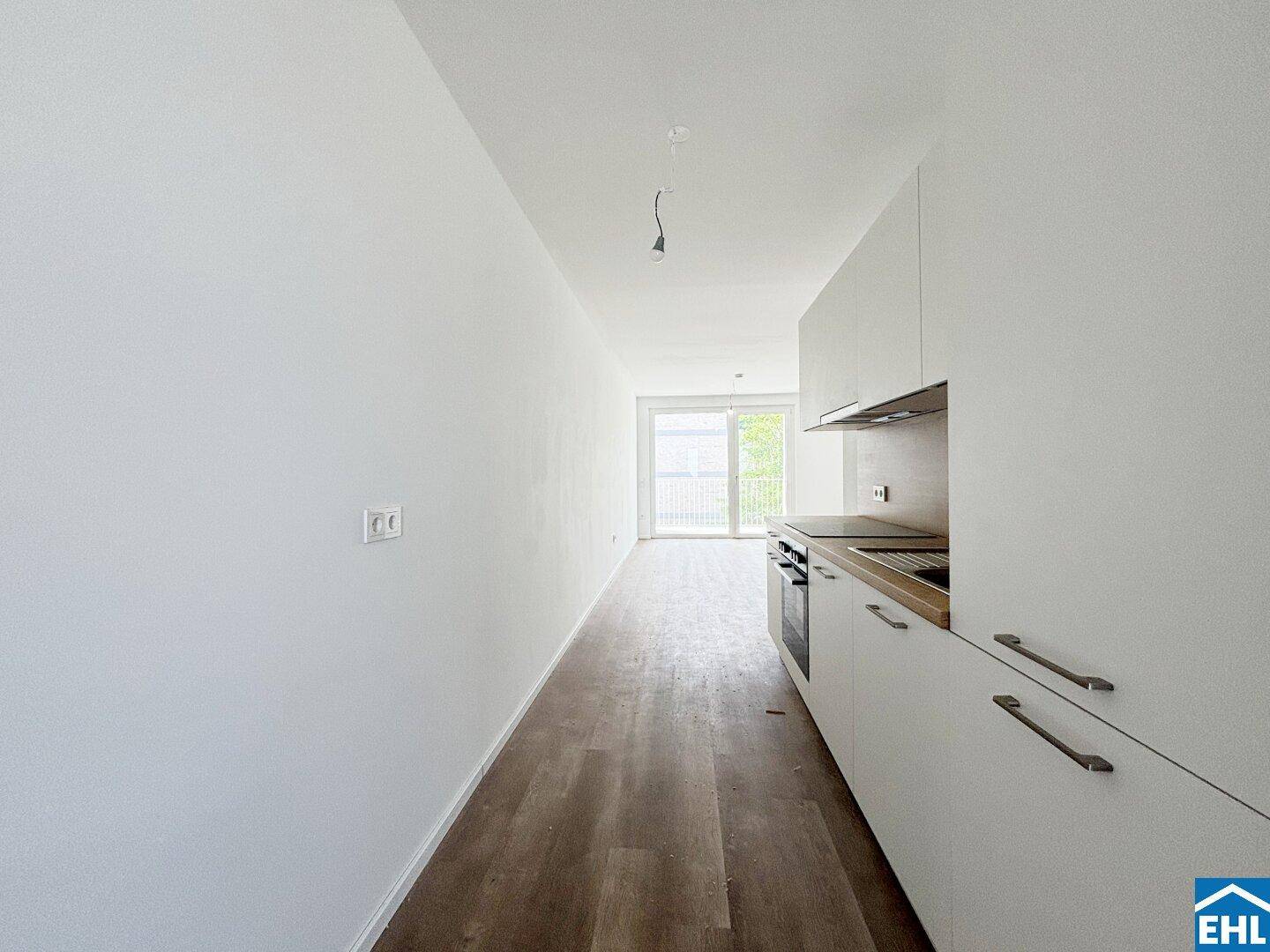 Moderner Küchenbereich mit weißen Einbauschränken und Zugang zum Balkon.