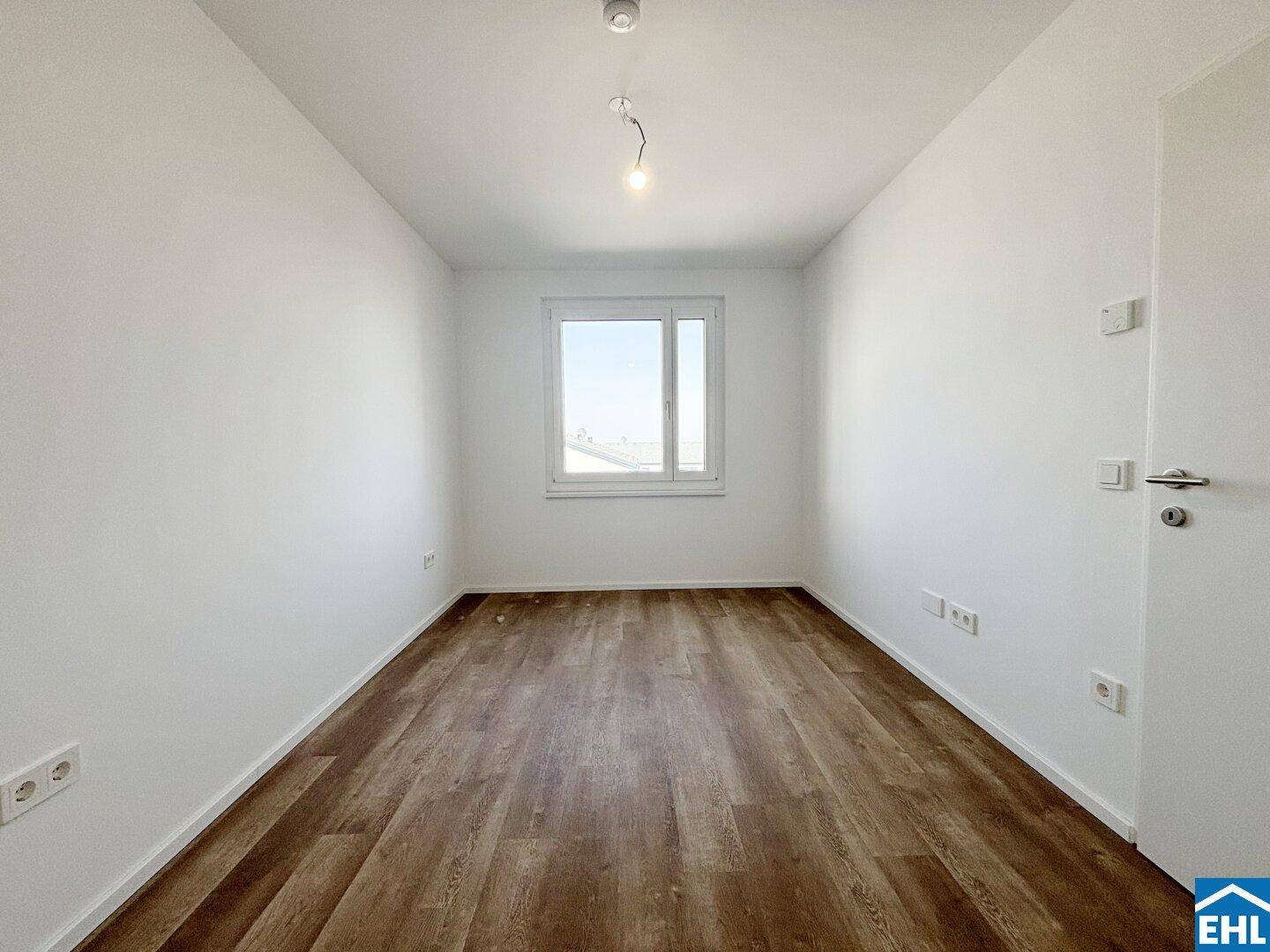 Schlafzimmer mit Laminatboden und einem großen Fenster, das viel Licht hereinlässt.