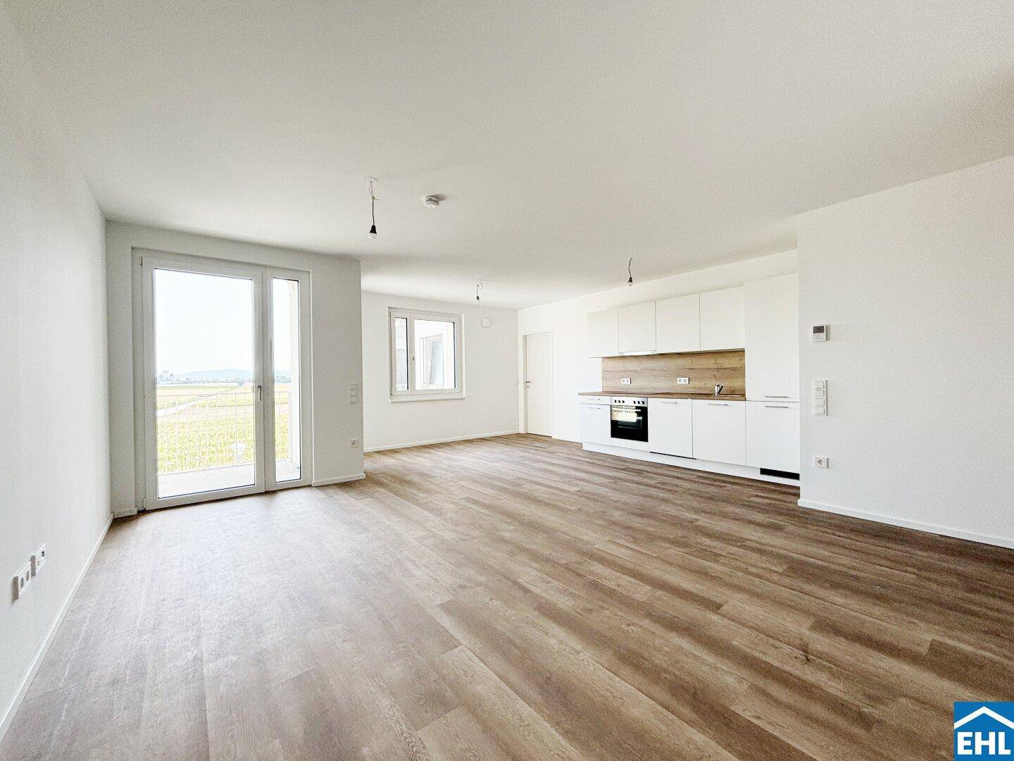 Heller, offener Wohnbereich mit Laminatboden und Zugang zum Balkon.